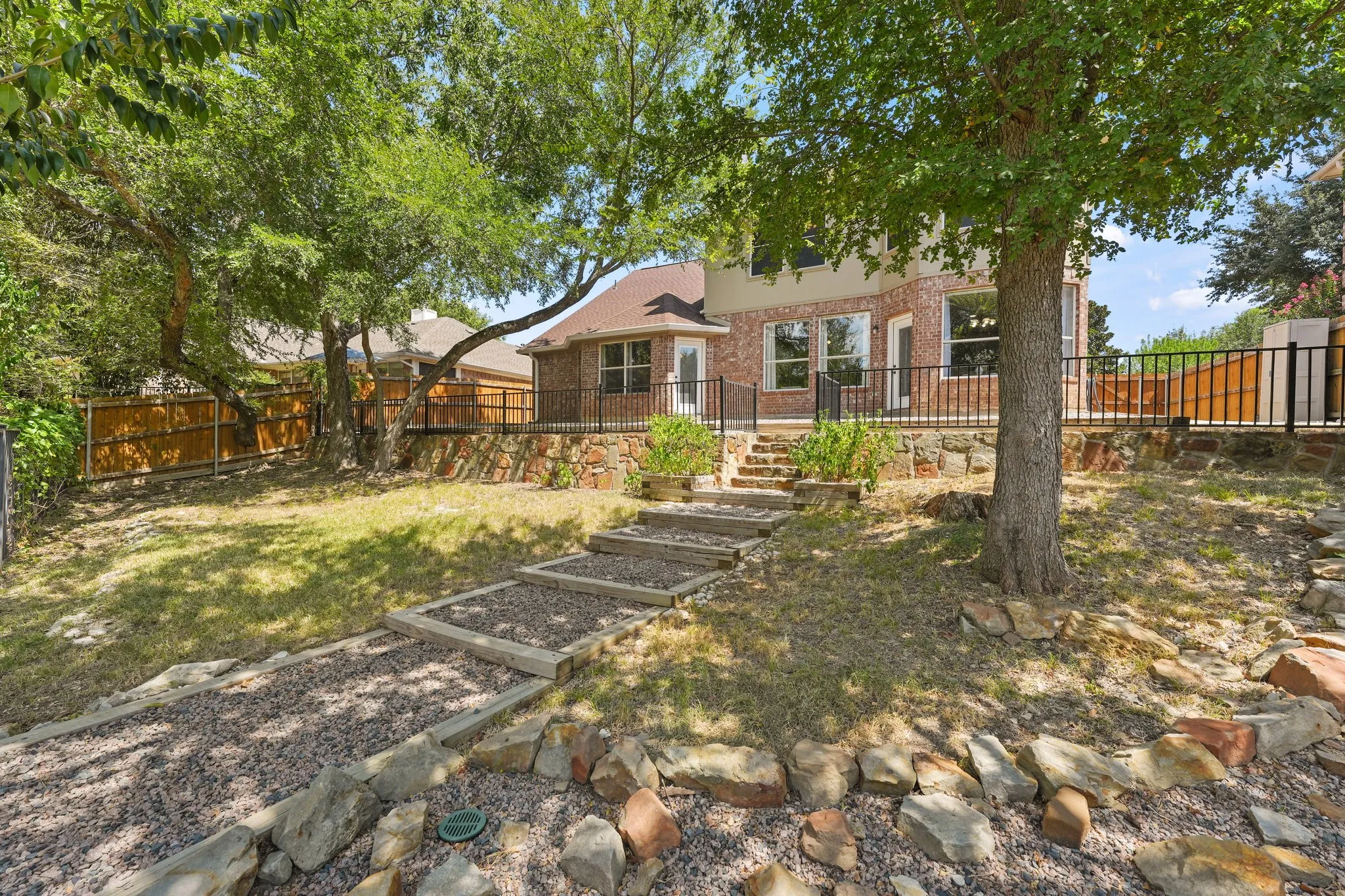 Tiered backyard featuring a gravel path with wood borders, stone retaining wall, and mature trees