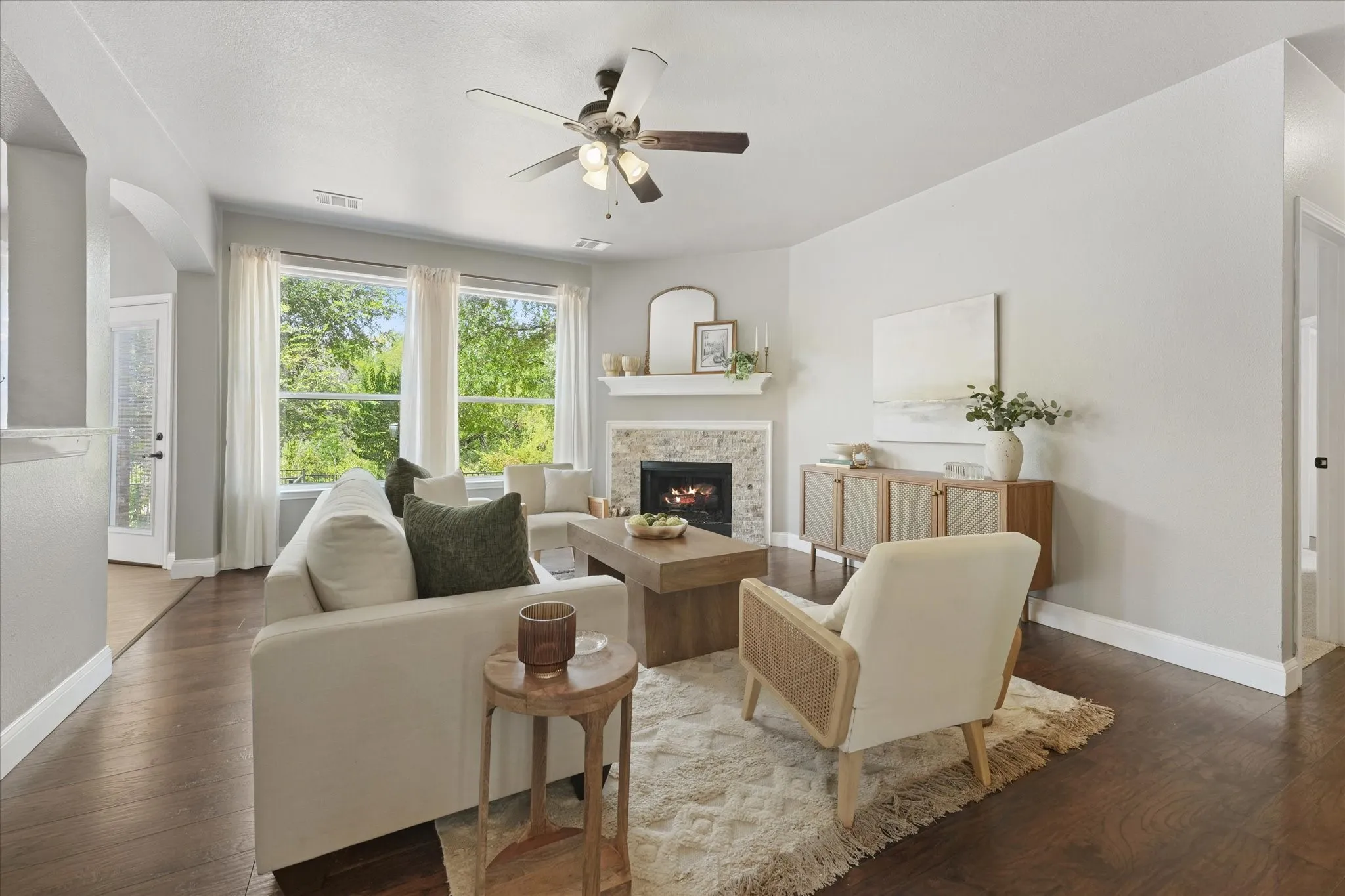Spacious living area featuring wood-finish flooring, a stone-surround fireplace with a mantel, and a ceiling fan