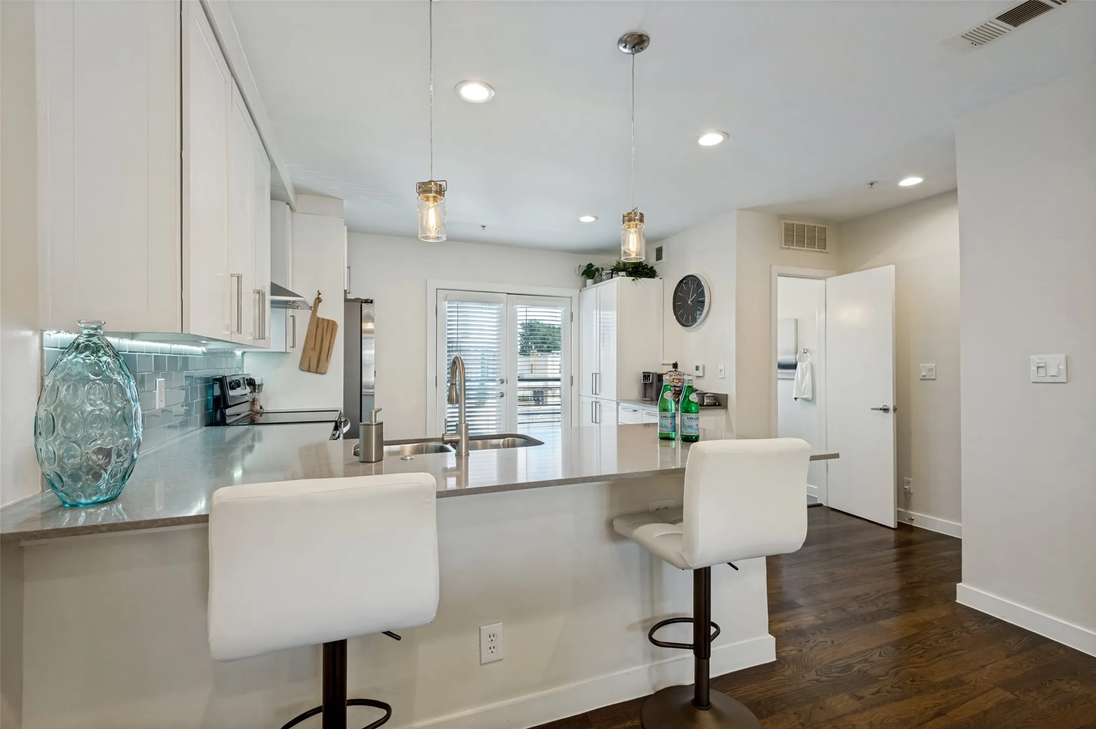 Kitchen featuring a breakfast bar with stone countertop, white cabinetry, under-cabinet lighting, and glass tile backsplash