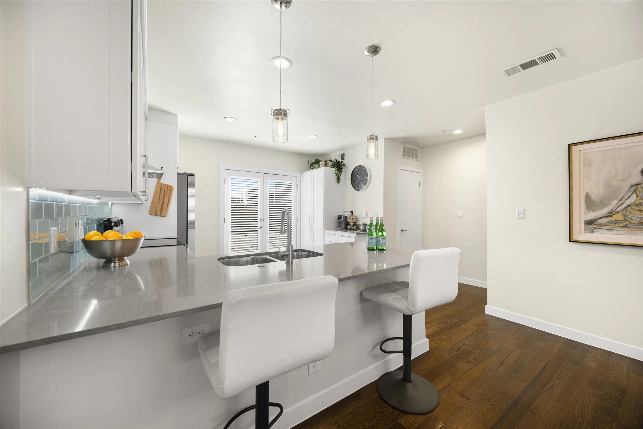 Modern kitchen featuring white cabinetry, a large kitchen island with a double basin sink, and pendant lighting