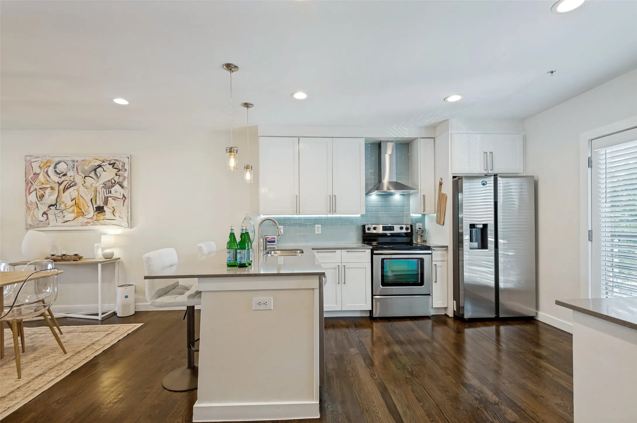 Kitchen featuring dark wood-finish flooring, stainless steel appliances, white cabinetry, a light blue tile backsplash, and recessed lighting