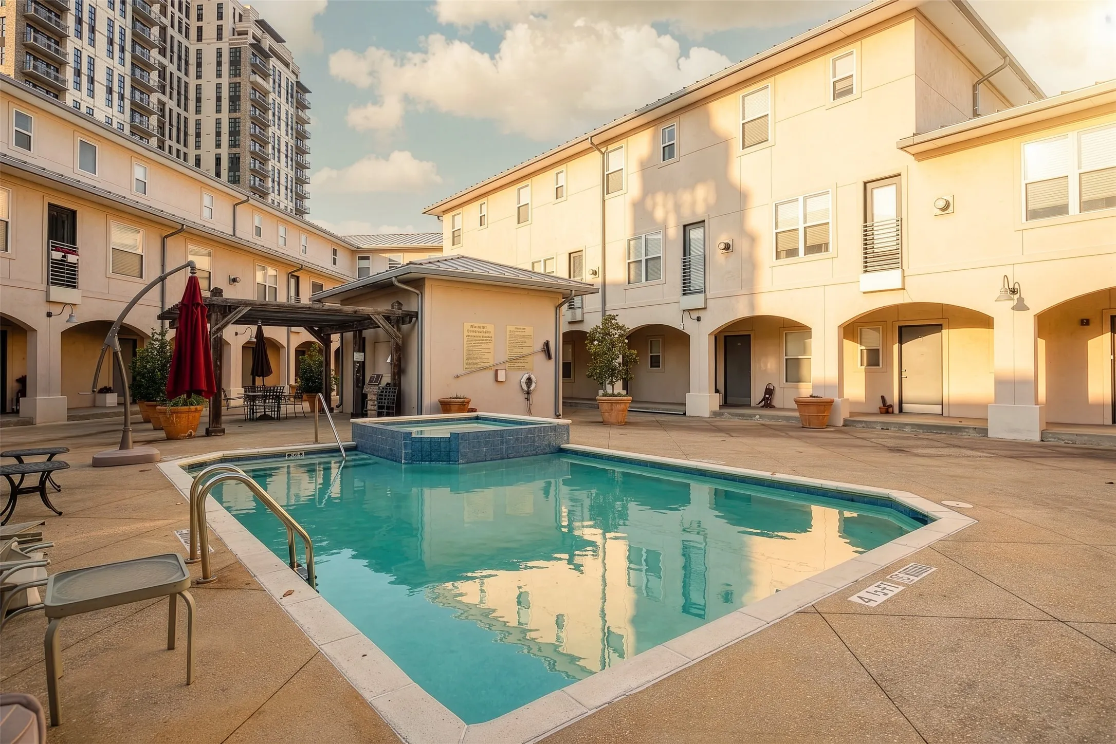 Community pool with an integrated spa, surrounded by concrete decking and archway-framed entrances