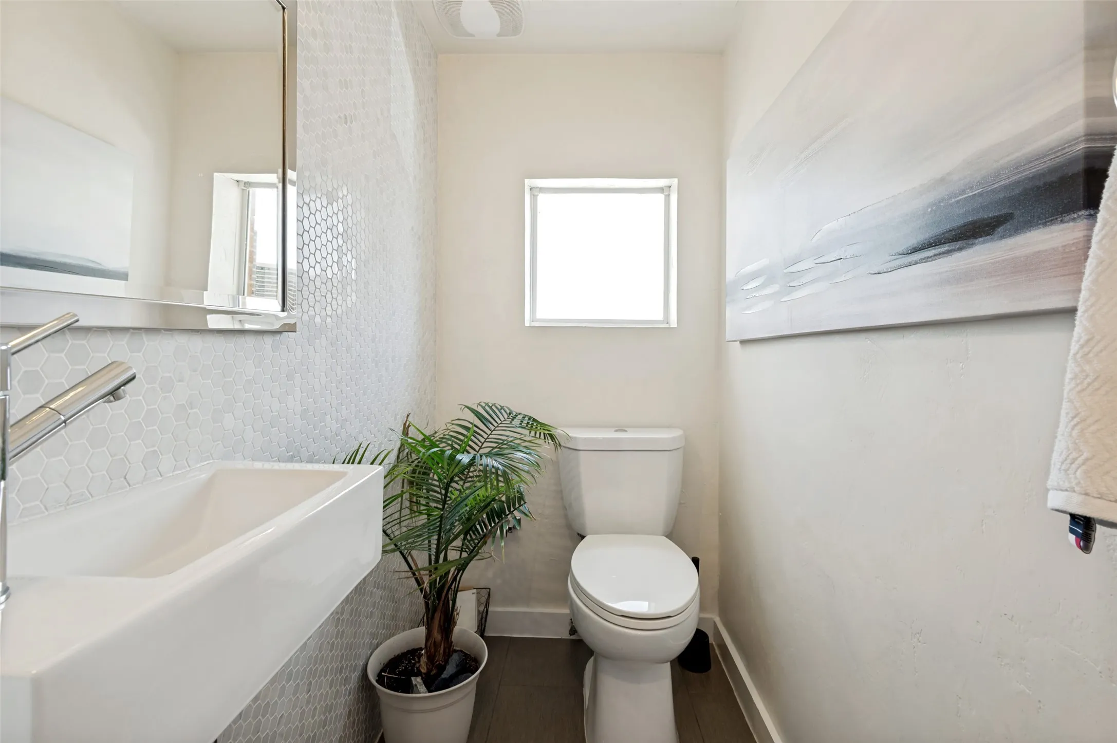 Floating vanity with integrated basin, hexagonal mosaic tile accent wall, chrome single-handle faucet, and wood-finish flooring