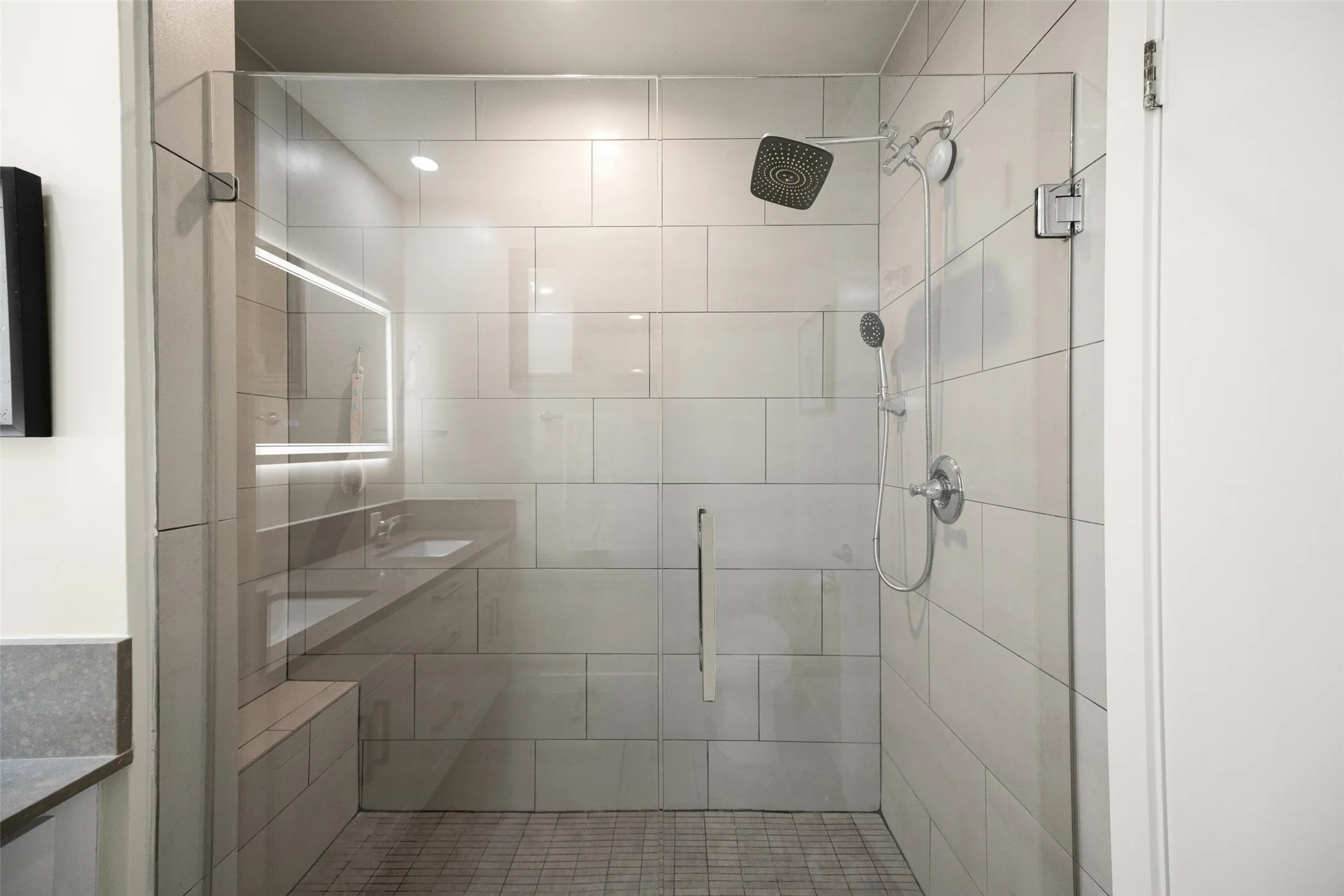 Glass-enclosed shower featuring a square rainfall shower head and a handheld spray