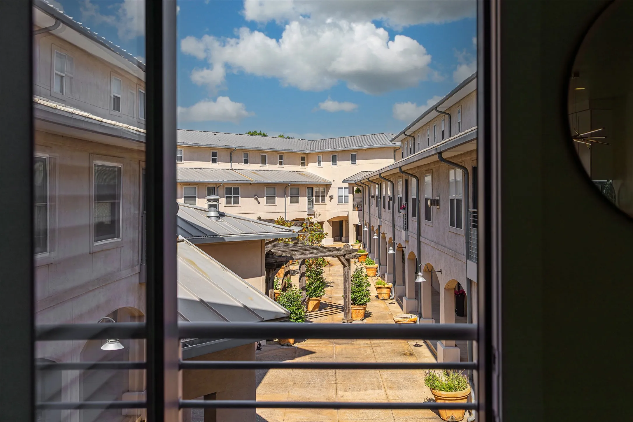 Courtyard perspective featuring an overhead pergola, numerous potted plantings, and arched walkways
