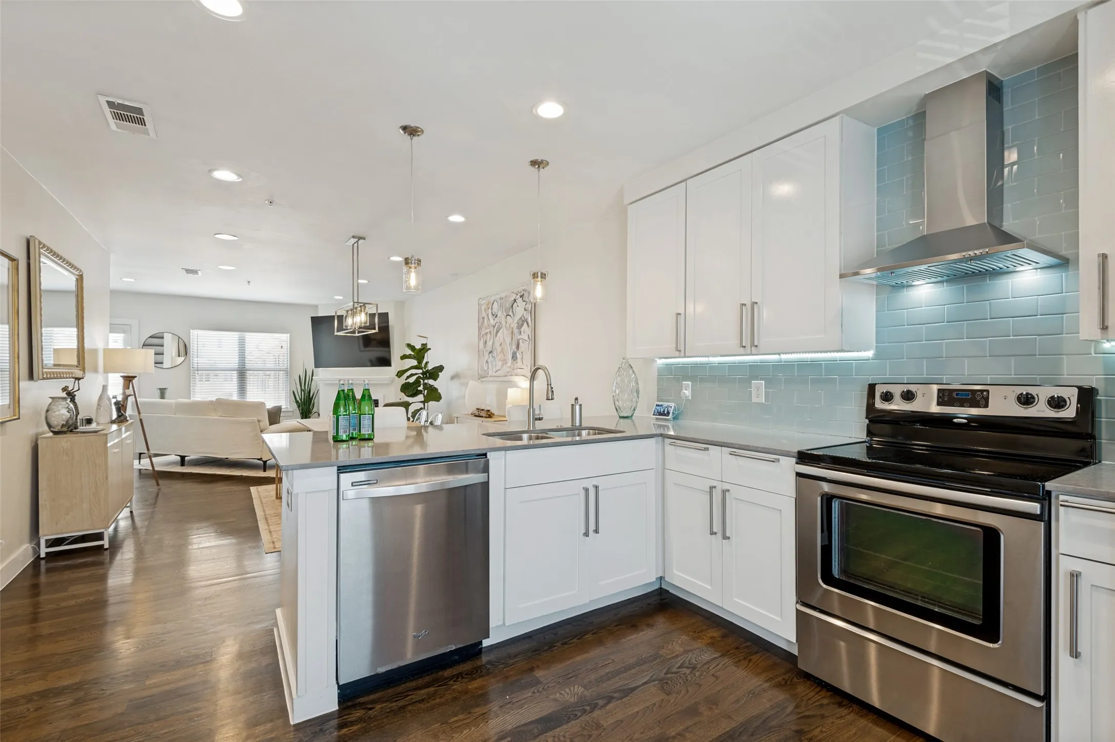 Modern kitchen featuring white cabinetry, stainless steel appliances, light blue subway tile backsplash, and dark wood-finish flooring