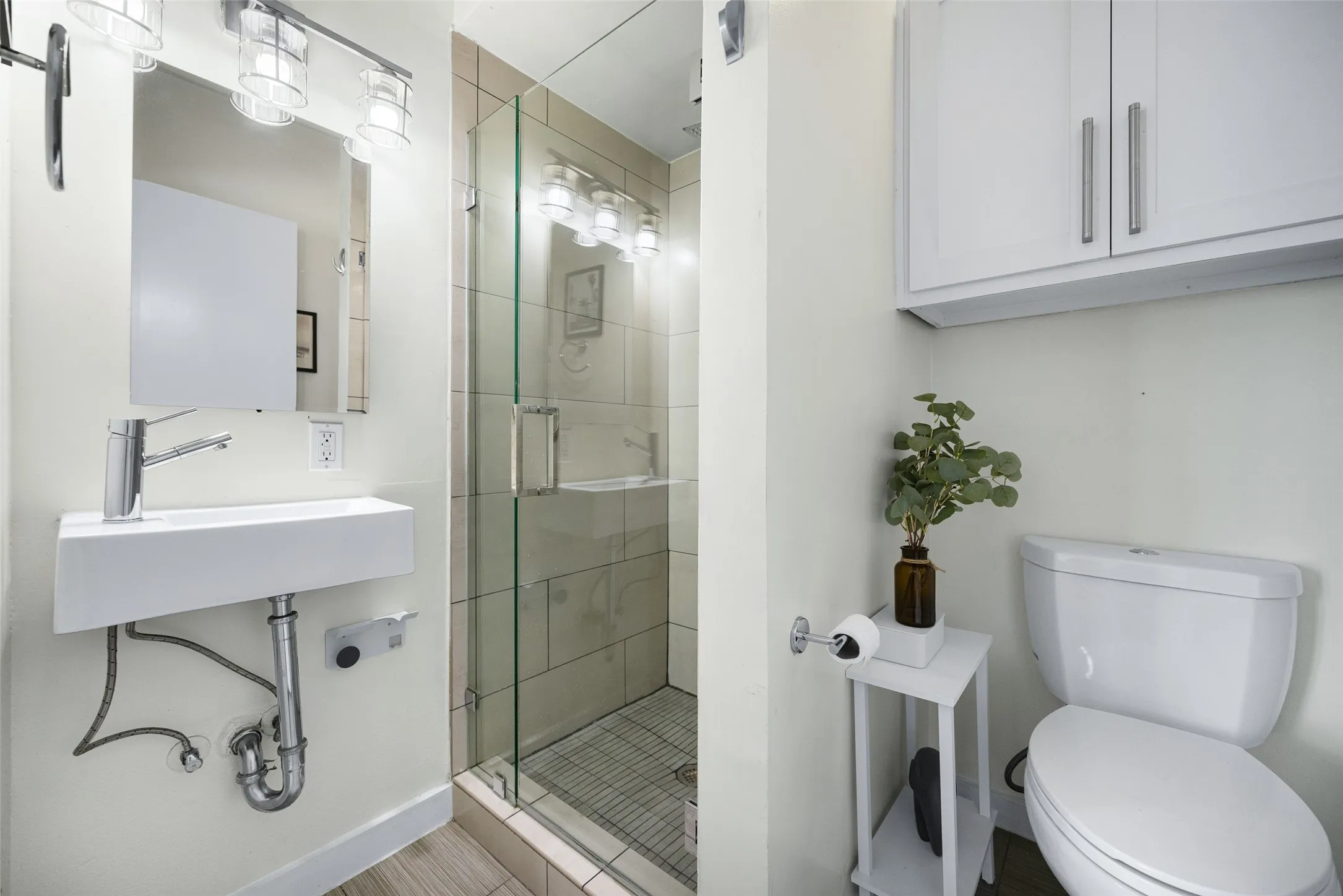 White floating vanity with a chrome faucet, illuminated mirror, and glass-enclosed shower with tiled walls