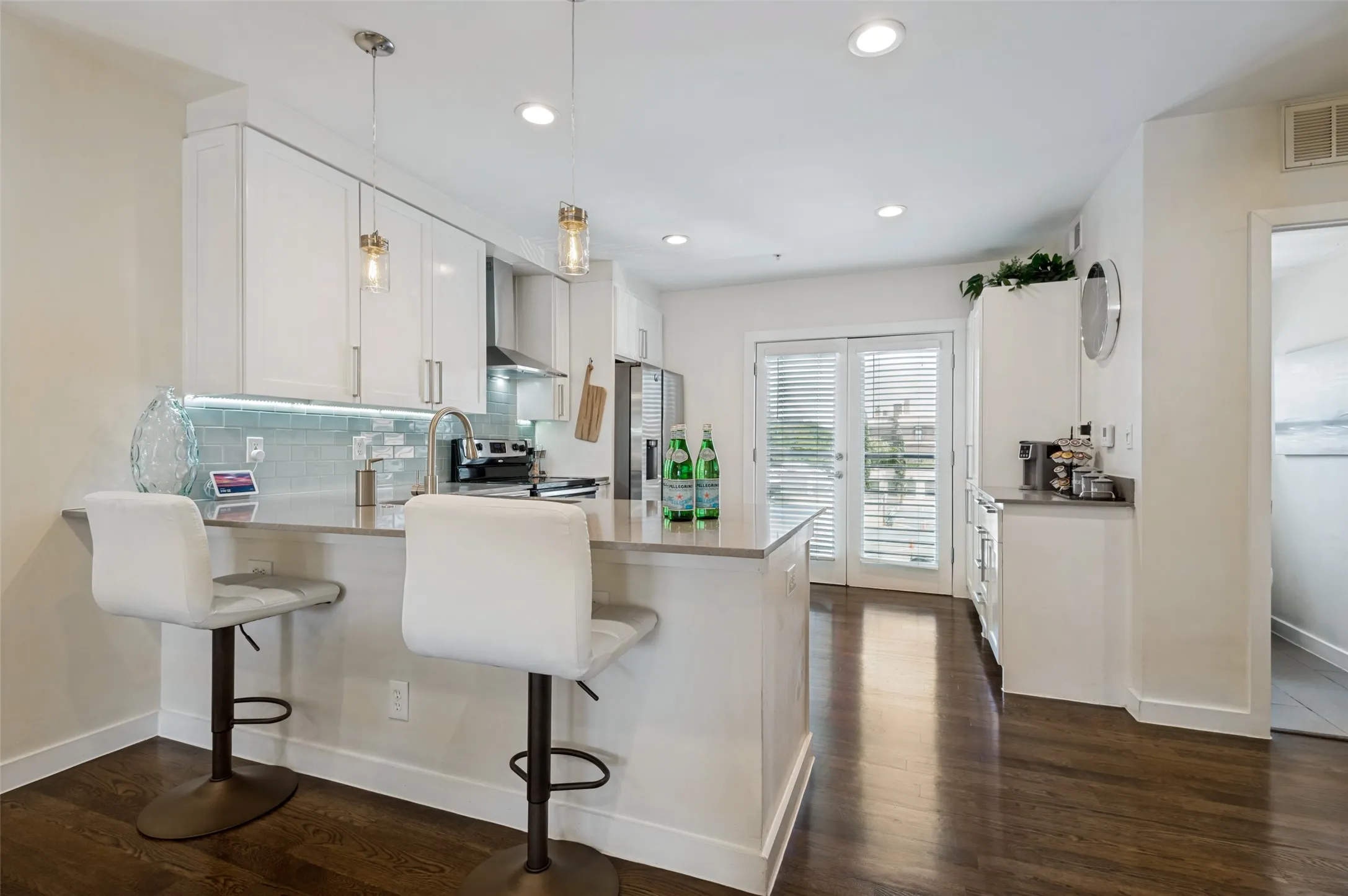 Kitchen featuring white cabinetry, stainless steel appliances, a light-toned backsplash, a breakfast bar with pendant lighting, and dark wood-finish flooring