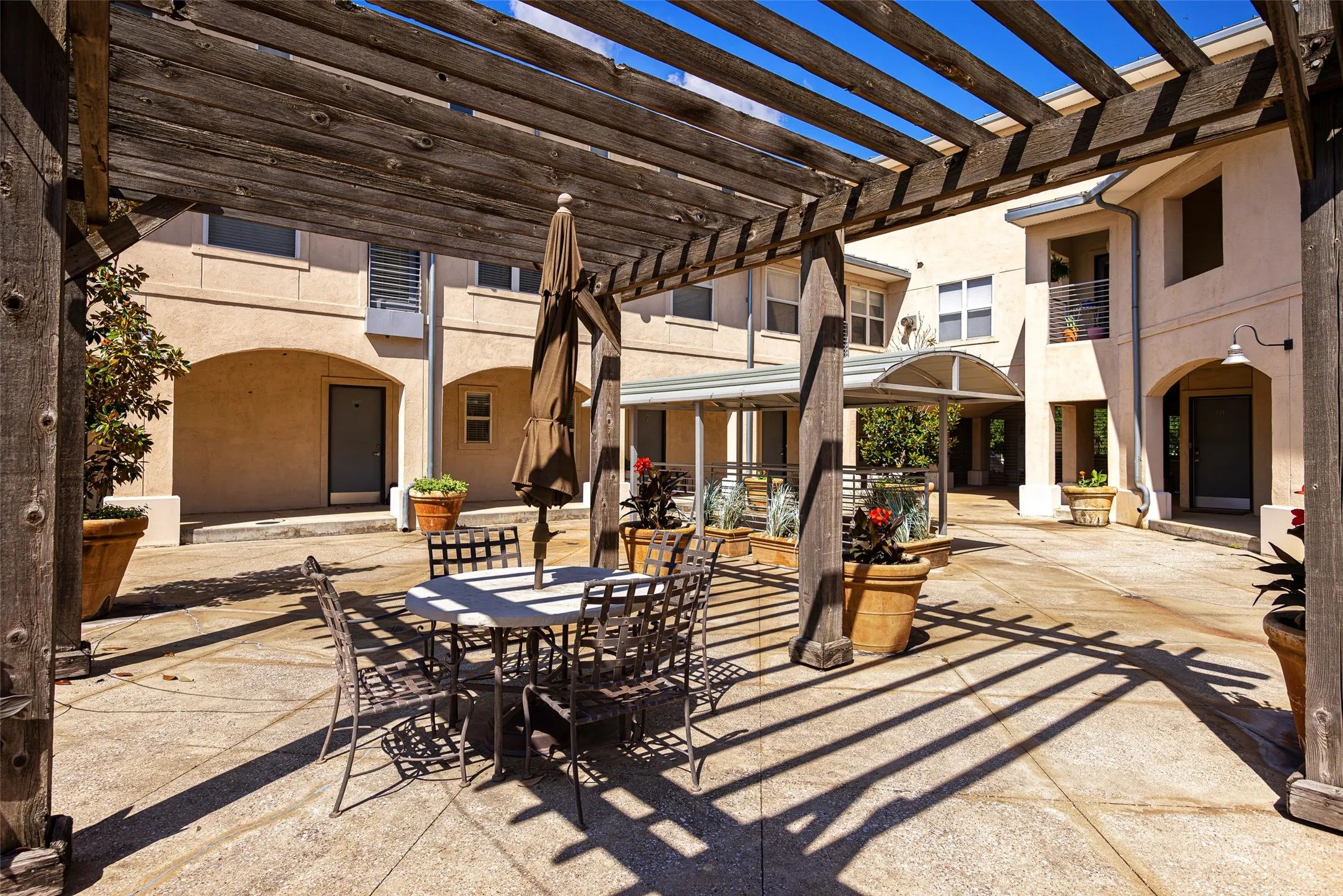 Expansive outdoor courtyard featuring a large wooden pergola, concrete paver flooring, and arched architectural details