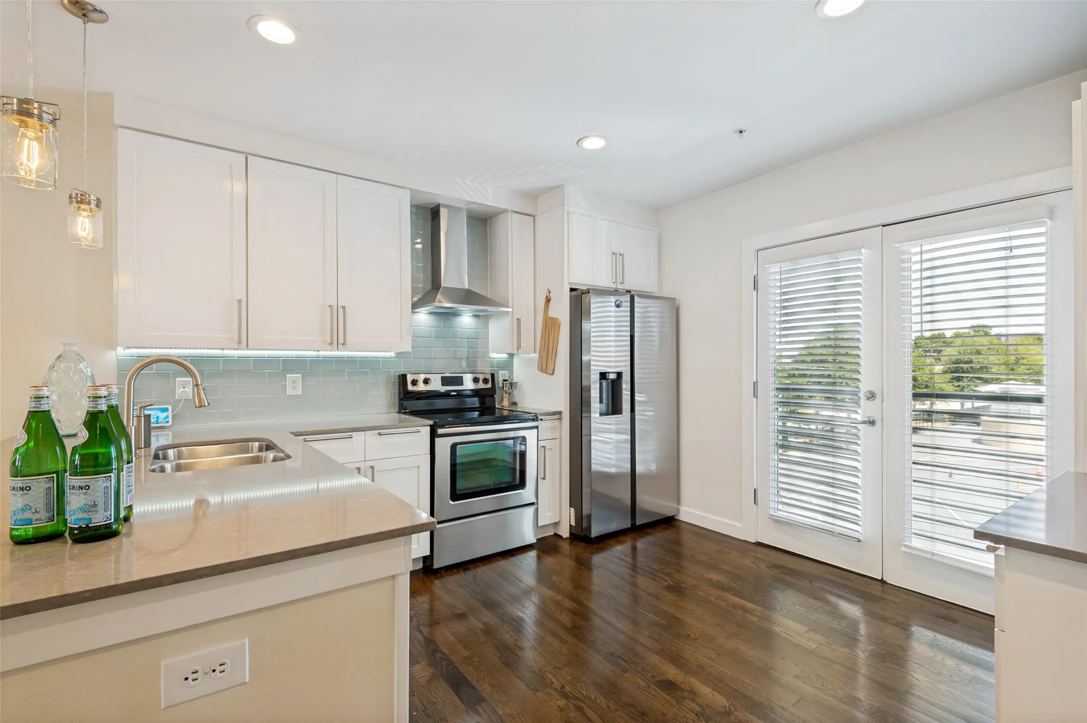 Kitchen featuring white cabinetry, stainless steel appliances, a light blue tile backsplash, wood-finish flooring, and double French doors