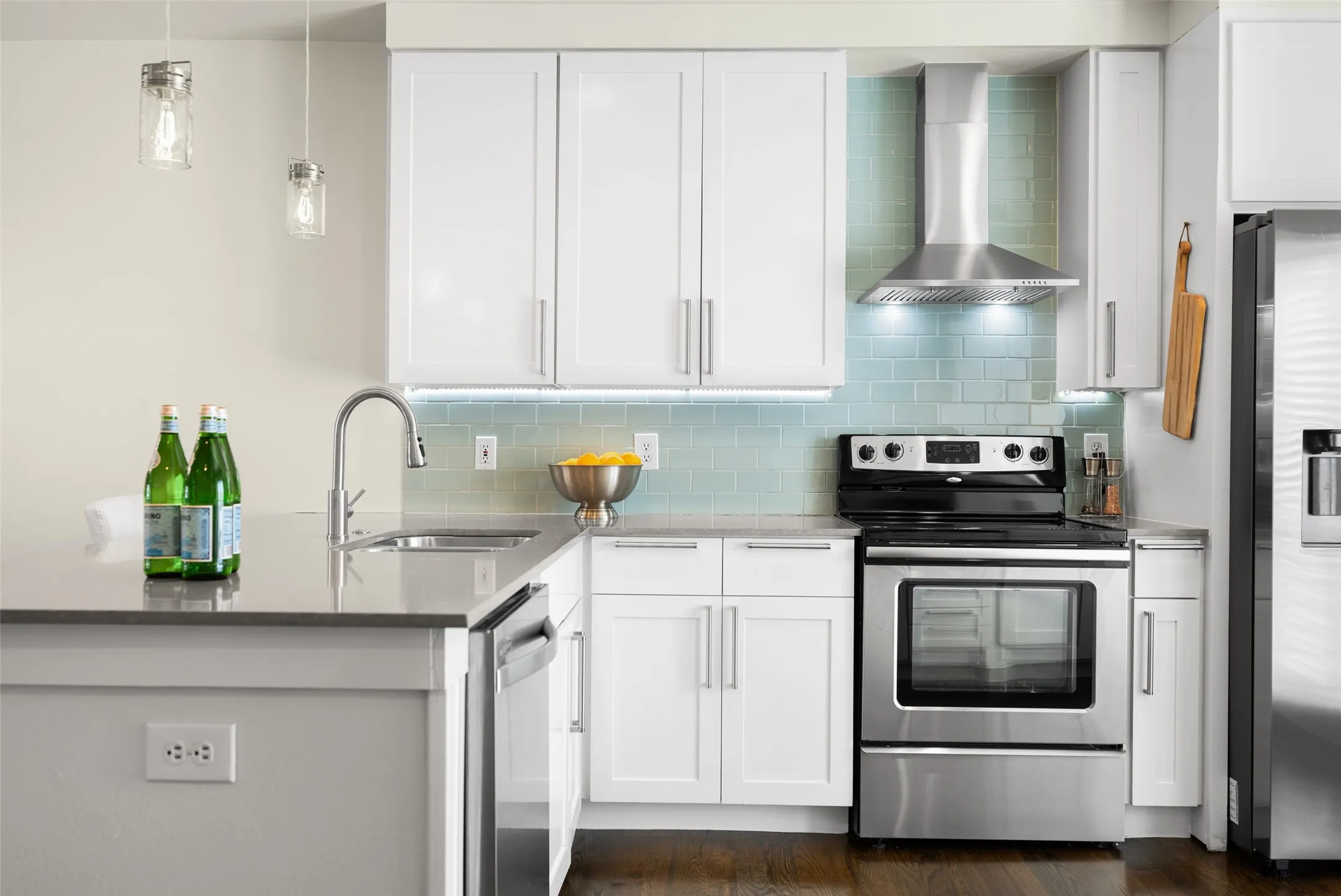 Modern kitchen featuring white shaker cabinetry, stainless steel appliances, a light blue subway tile backsplash, a stainless steel range hood, and pendant lighting