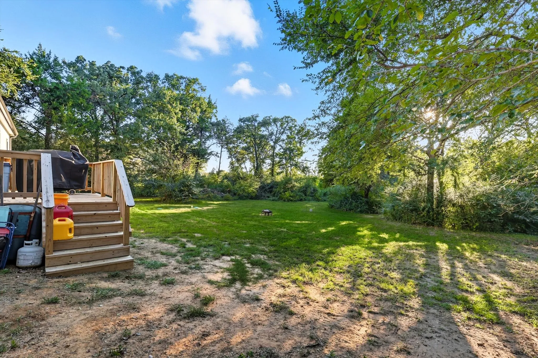 View of grassy yard featuring a deck, a playground, and view of scattered trees