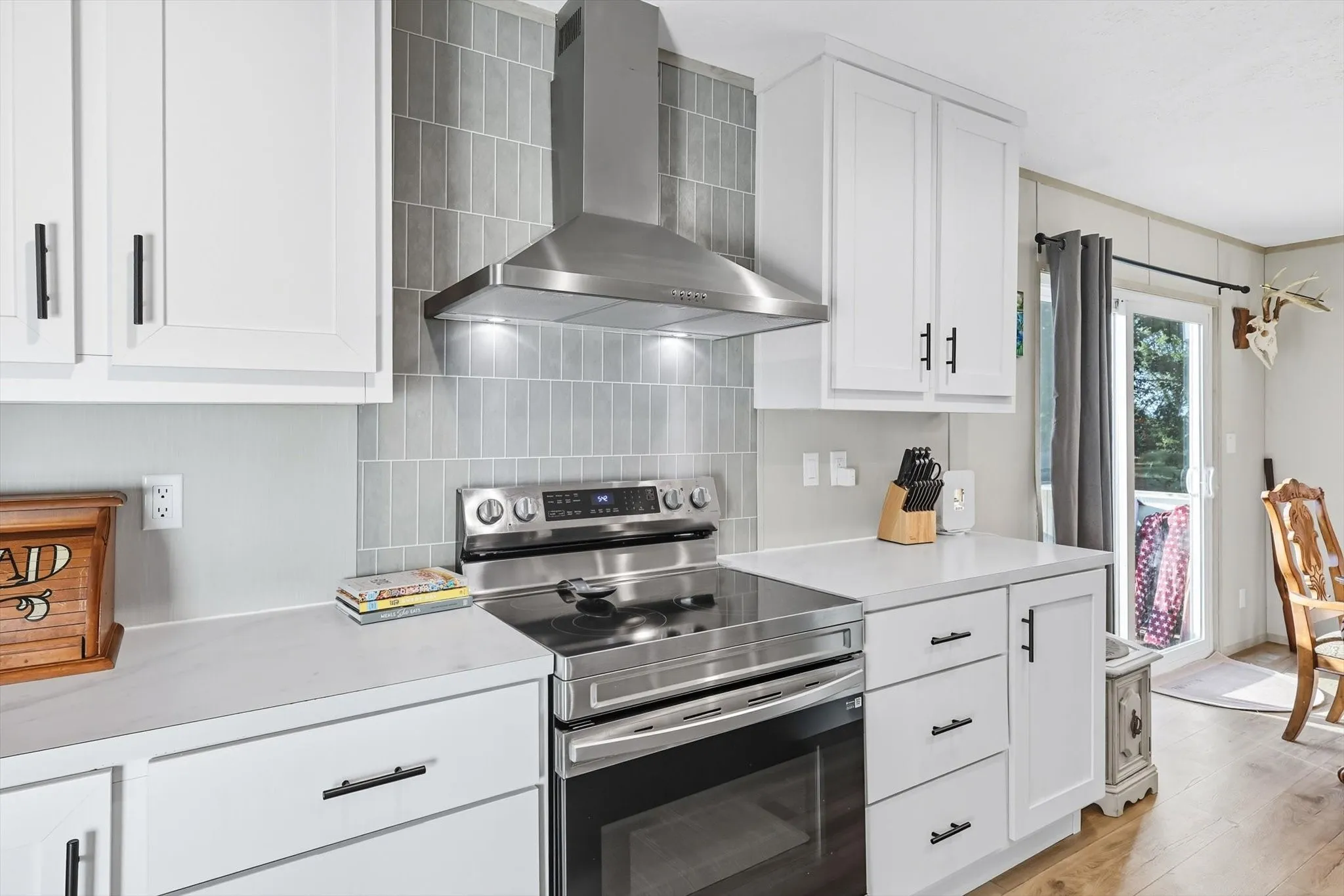 Kitchen featuring stainless steel electric range, wall chimney exhaust hood, white cabinets, and light countertops