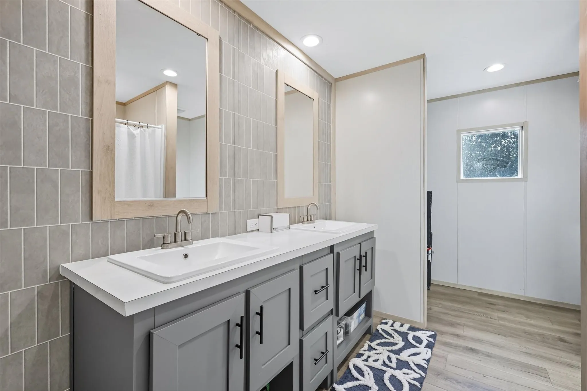 Full bath with double vanity, light wood-type flooring, tile walls, recessed lighting, and a shower with shower curtain