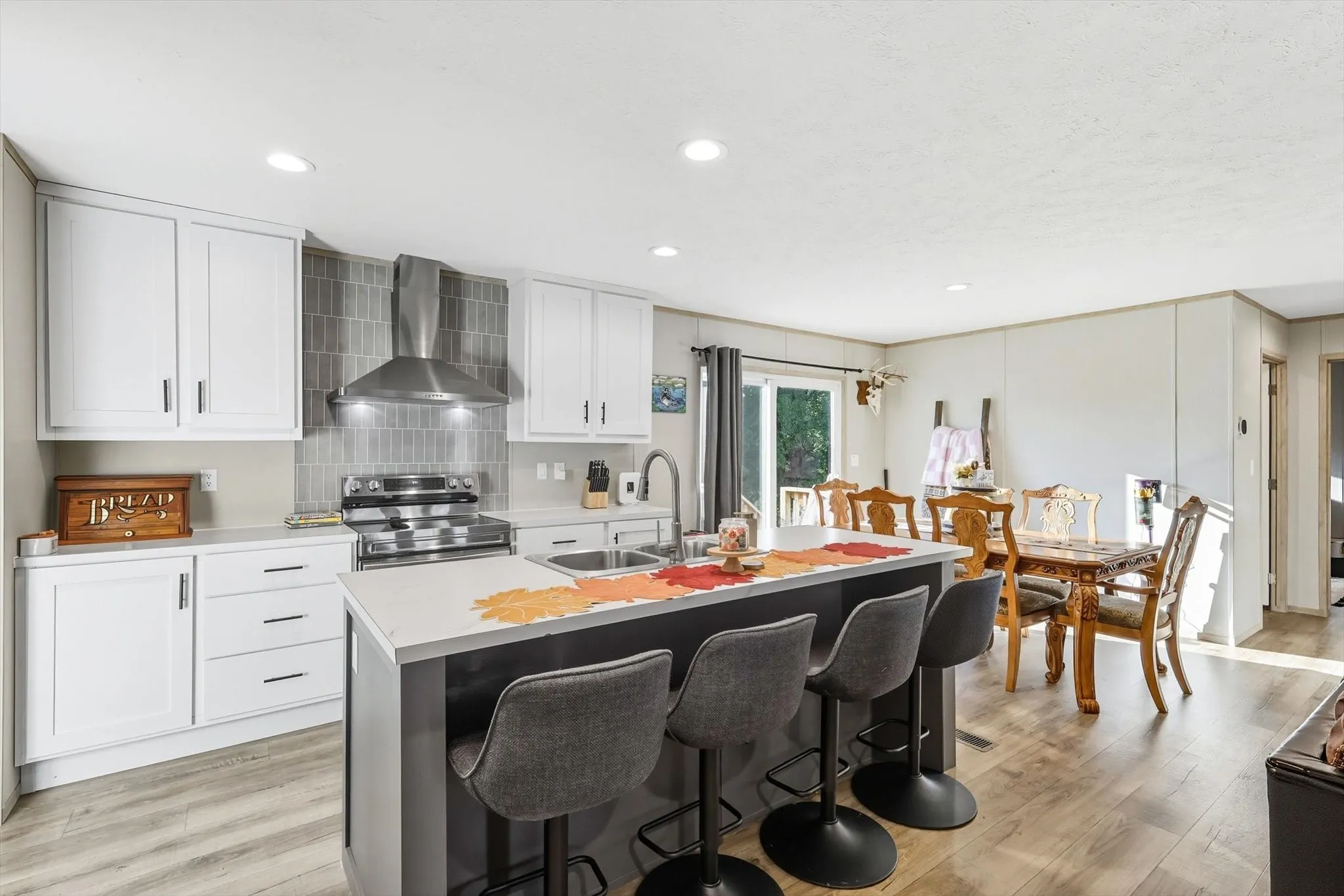 Kitchen featuring wall chimney range hood, light wood finished floors, electric range, light countertops, and recessed lighting