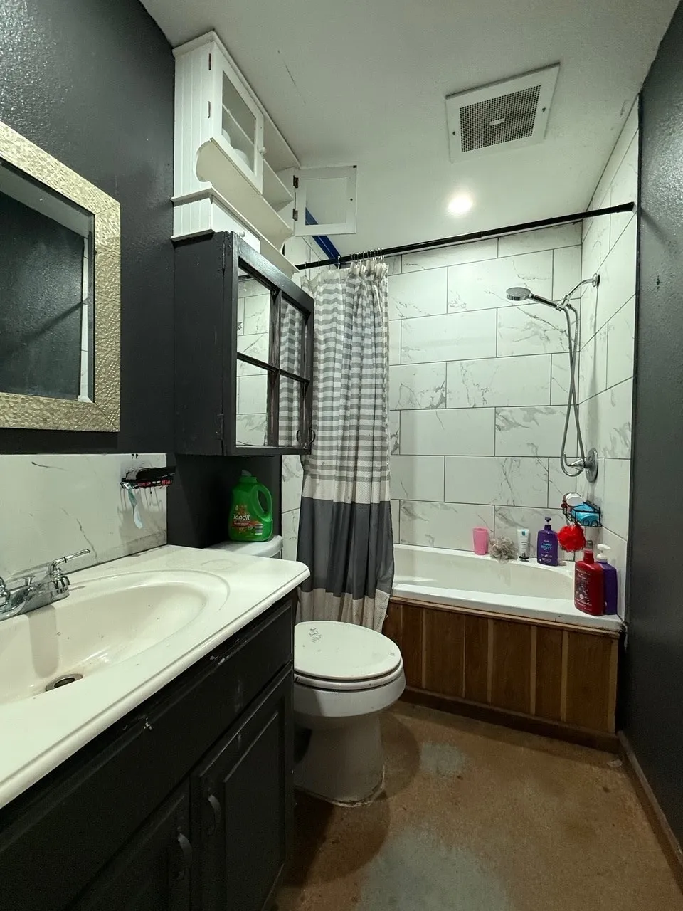 Bathroom featuring a standard white bathtub with a tiled surround, a white sink set in a dark vanity, and built-in white upper cabinetry