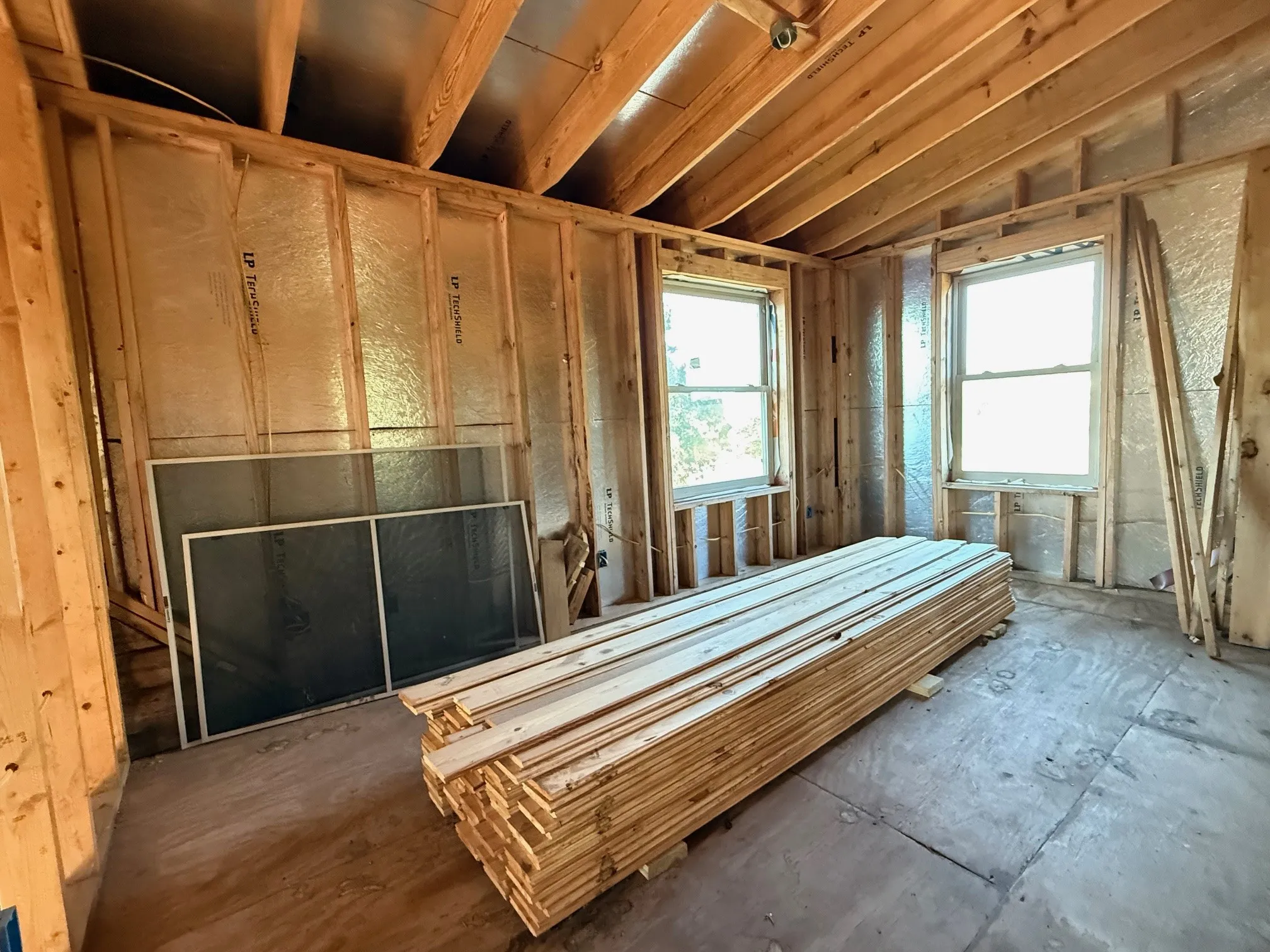 Unfinished interior space featuring exposed wood framing, two double-hung windows, and reflective insulation