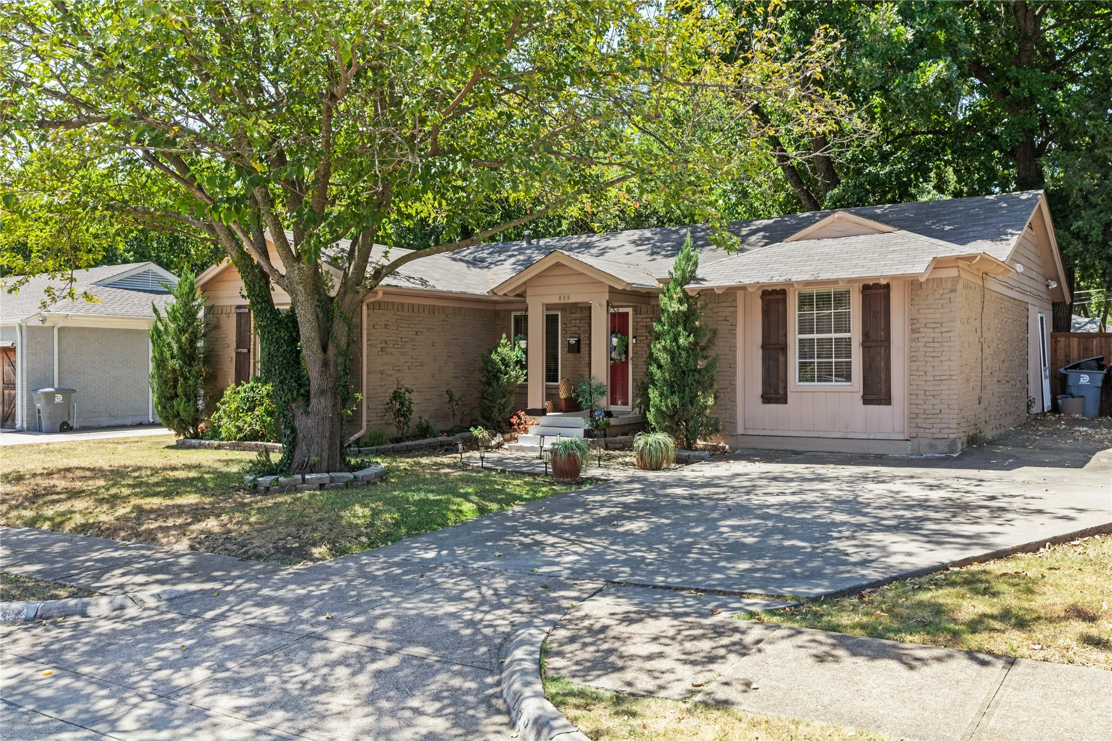Brick exterior with a gabled roofline, decorative window shutters, and a mature tree providing shade