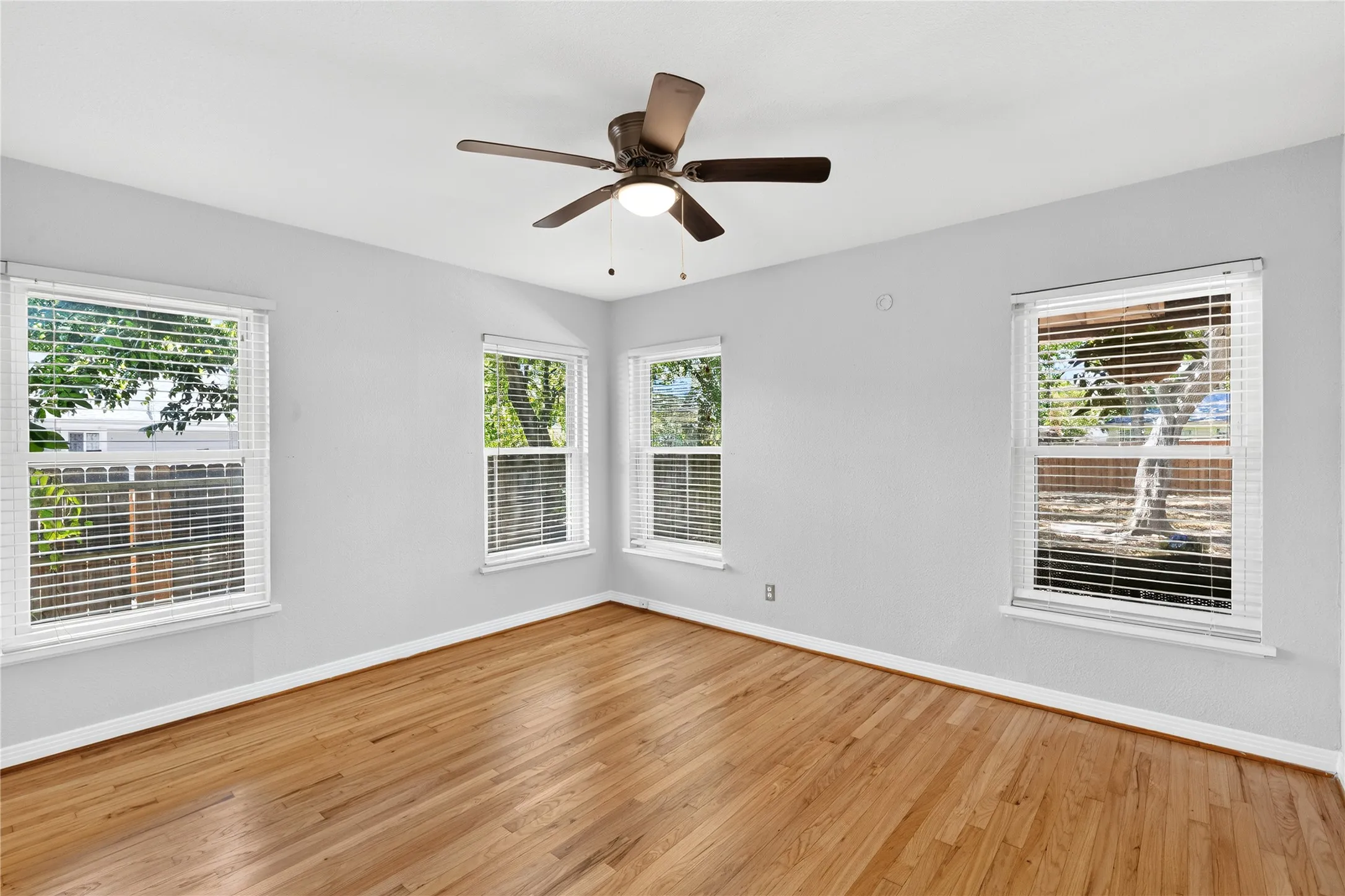 Hardwood flooring, multiple windows, ceiling fan with integrated lighting, neutral wall tones, and white trim