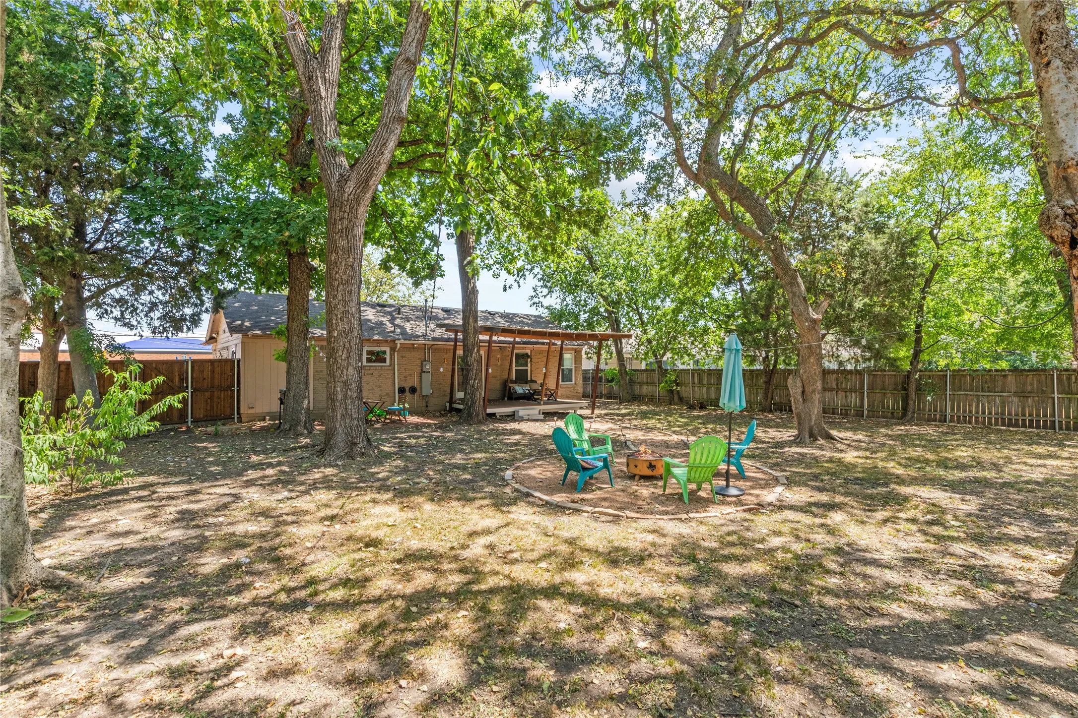 Spacious backyard with mature shade trees, a privacy fence, and a designated fire pit area