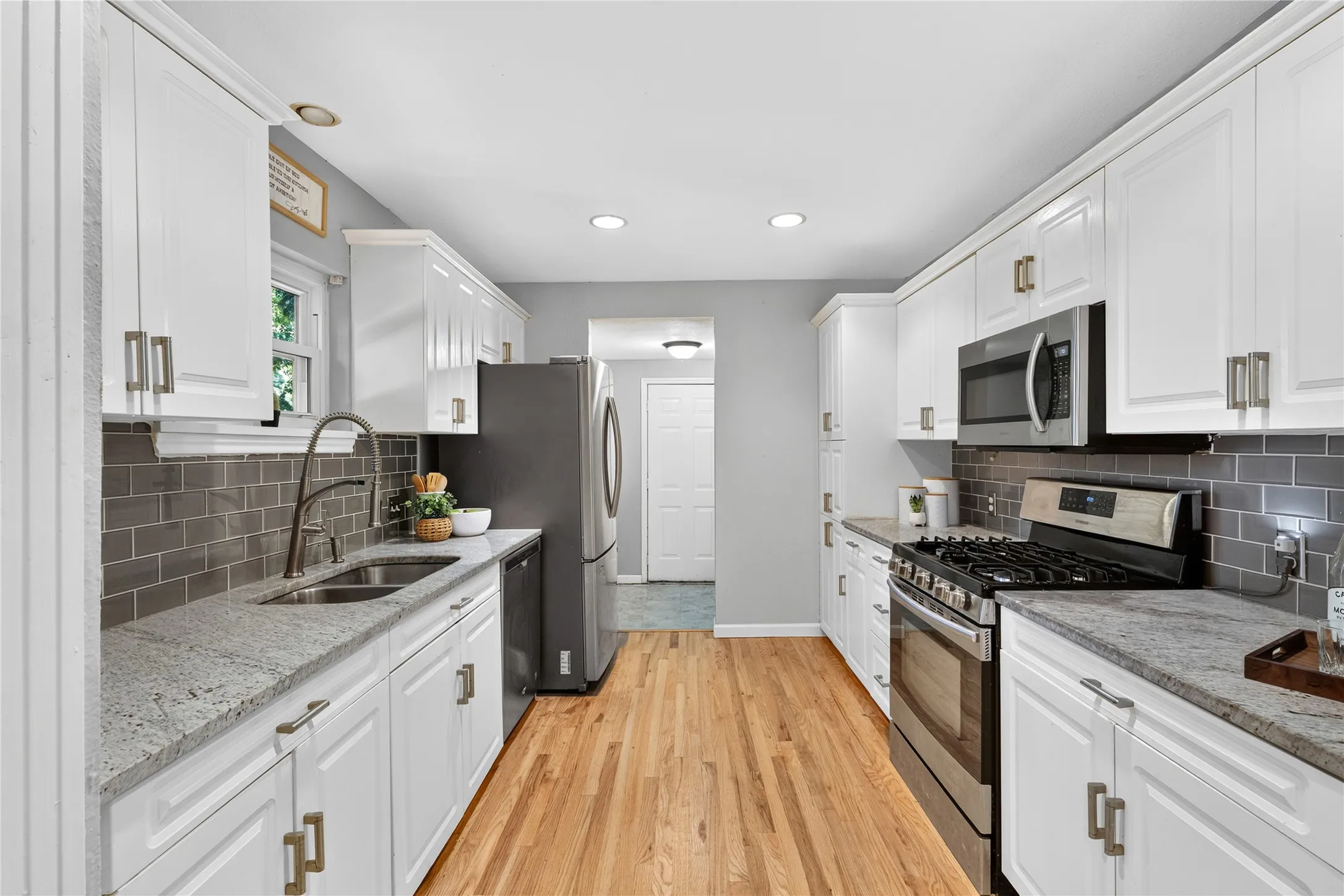White cabinetry with brushed nickel hardware, stainless steel appliances, light-toned wood-finish flooring, gray subway tile backsplash, and recessed lighting