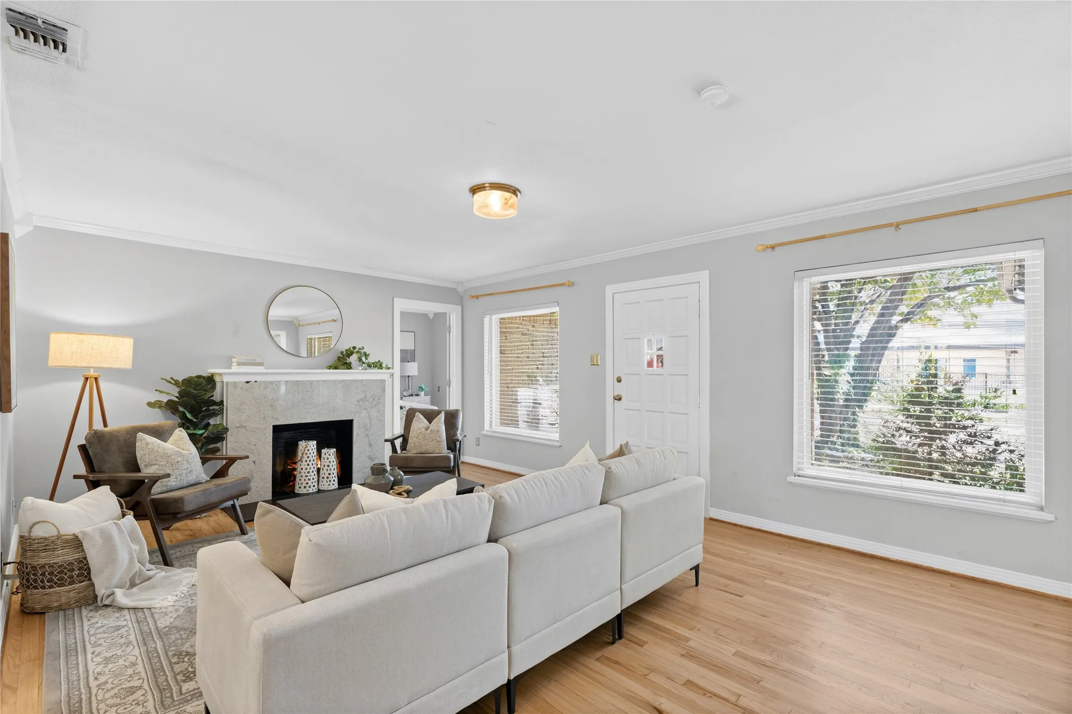 Living area featuring wood-finish flooring, a decorative fireplace with a stone surround, white crown molding, and multiple windows