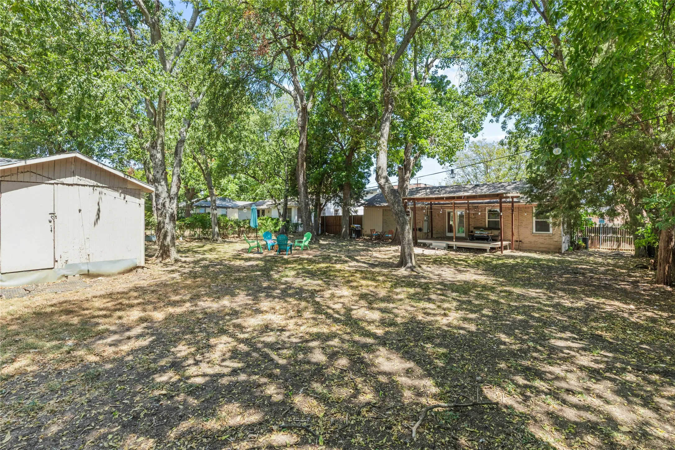 Expansive backyard space featuring mature trees, a detached storage shed, and a covered back patio with a wood deck