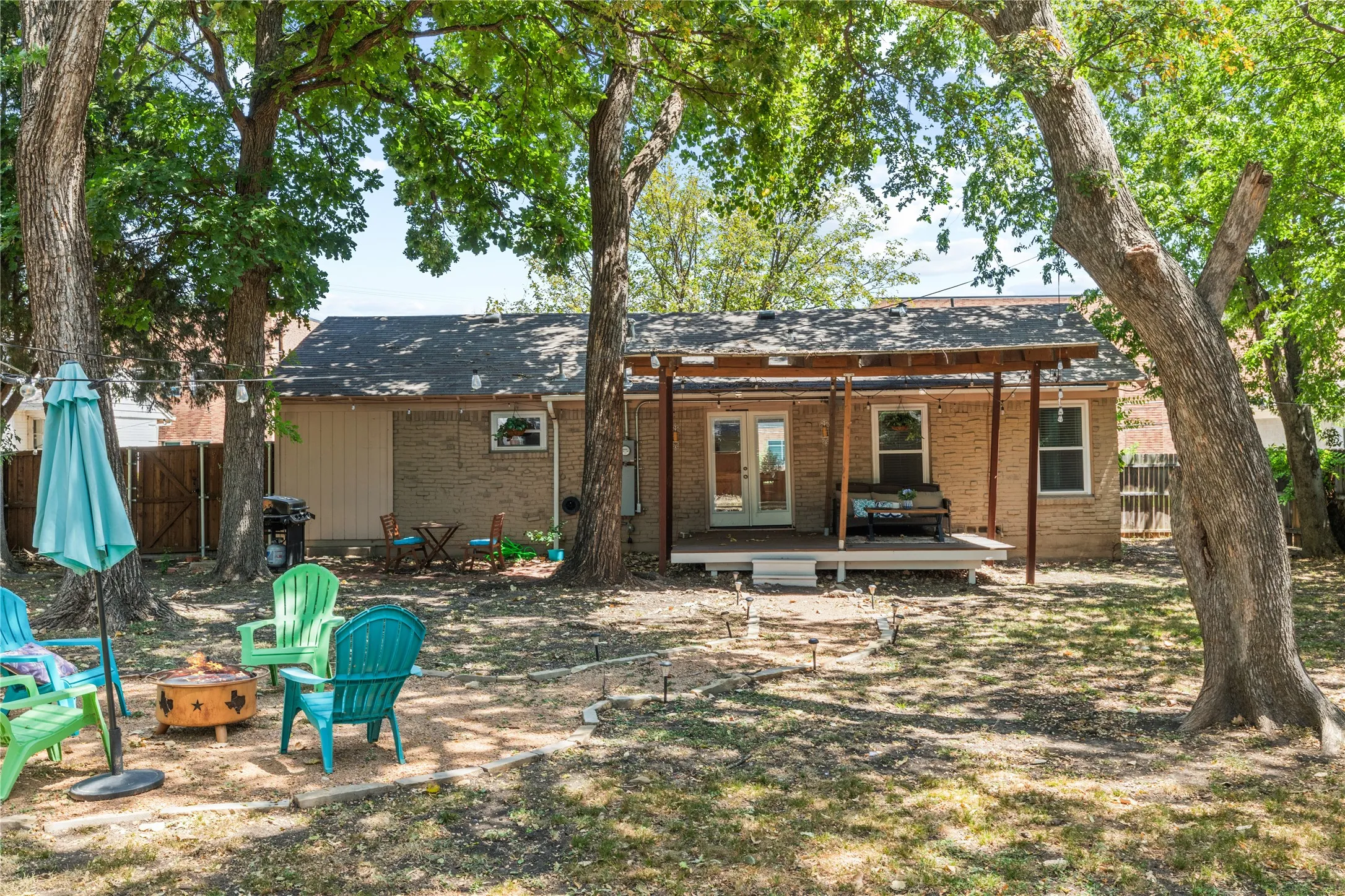 Brick exterior with a covered patio, multiple mature trees, and a wooden deck