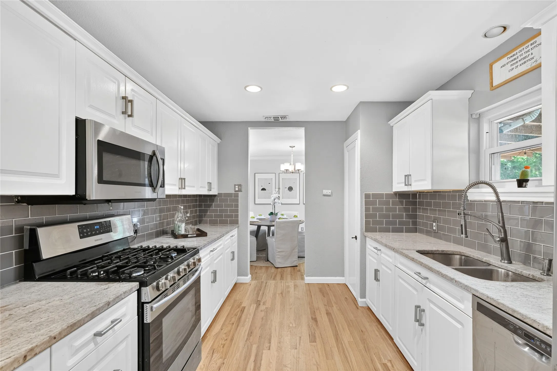 Galley kitchen featuring wood-finish flooring, white cabinetry with silver hardware, light-toned countertops, and a gray subway tile backsplash