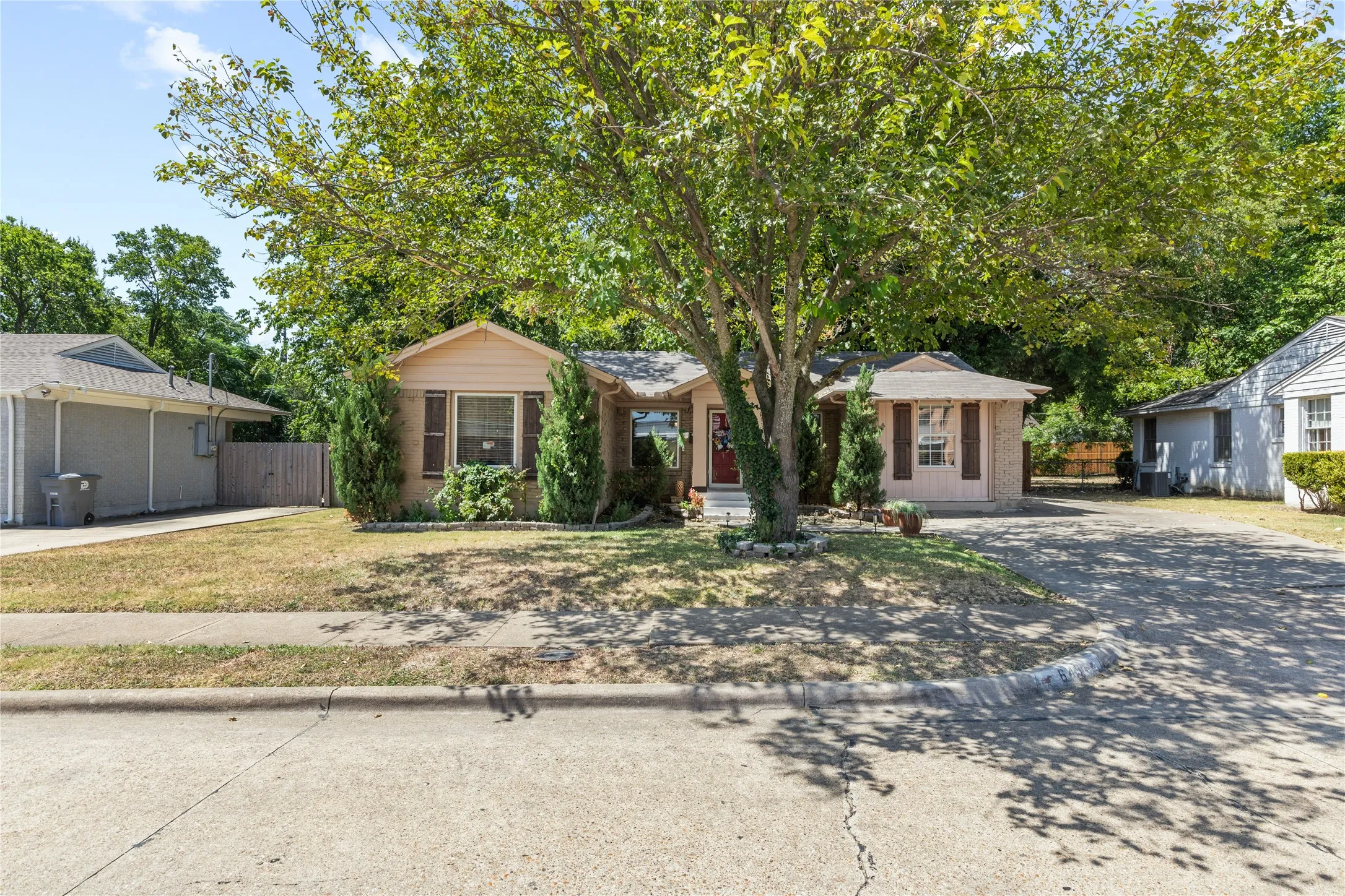 Brick veneer facade, covered entry, front landscaping, mature tree, and concrete driveway