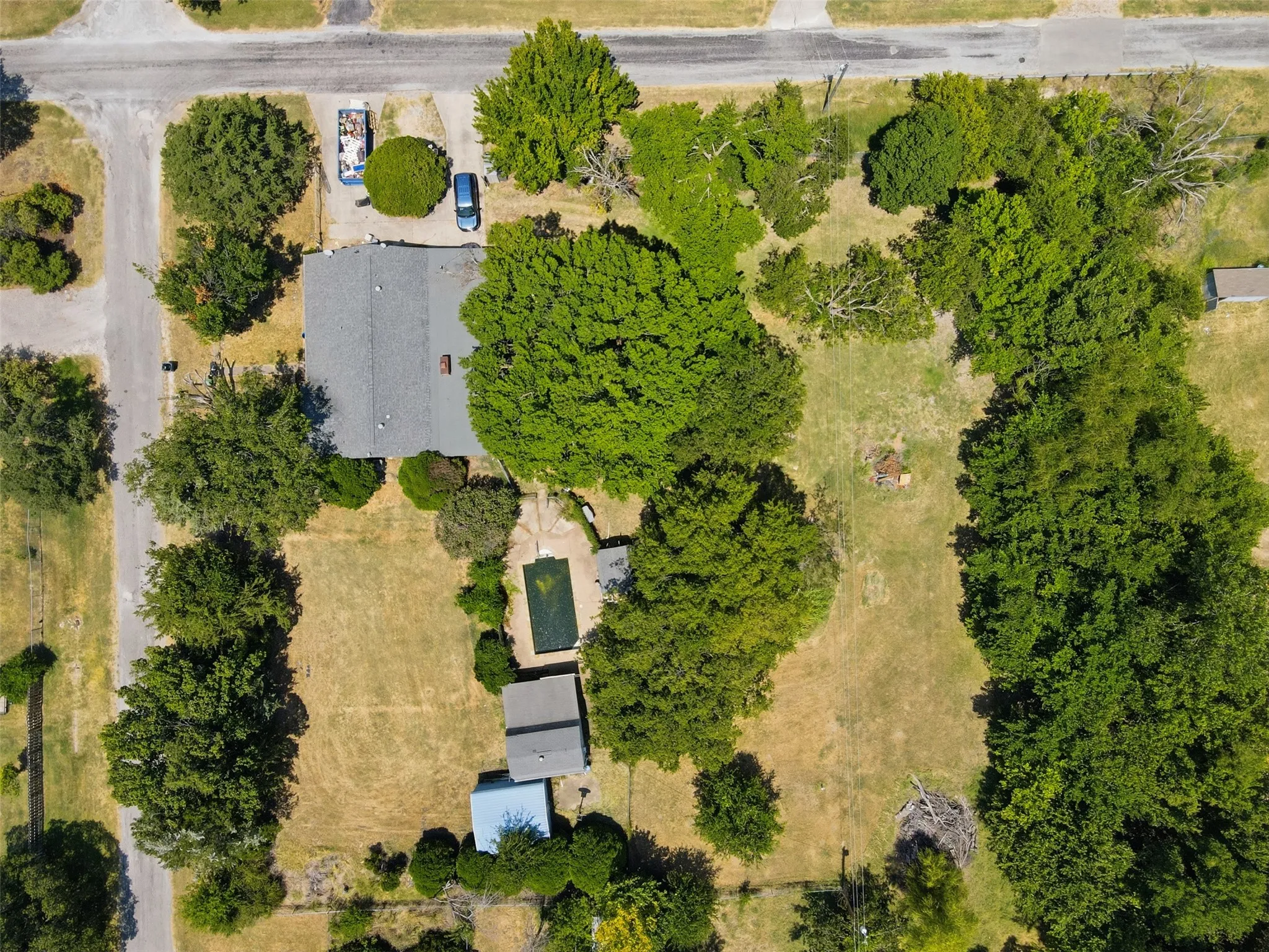 Expansive lot with mature trees, a detached storage building, and a rectangular in-ground pool