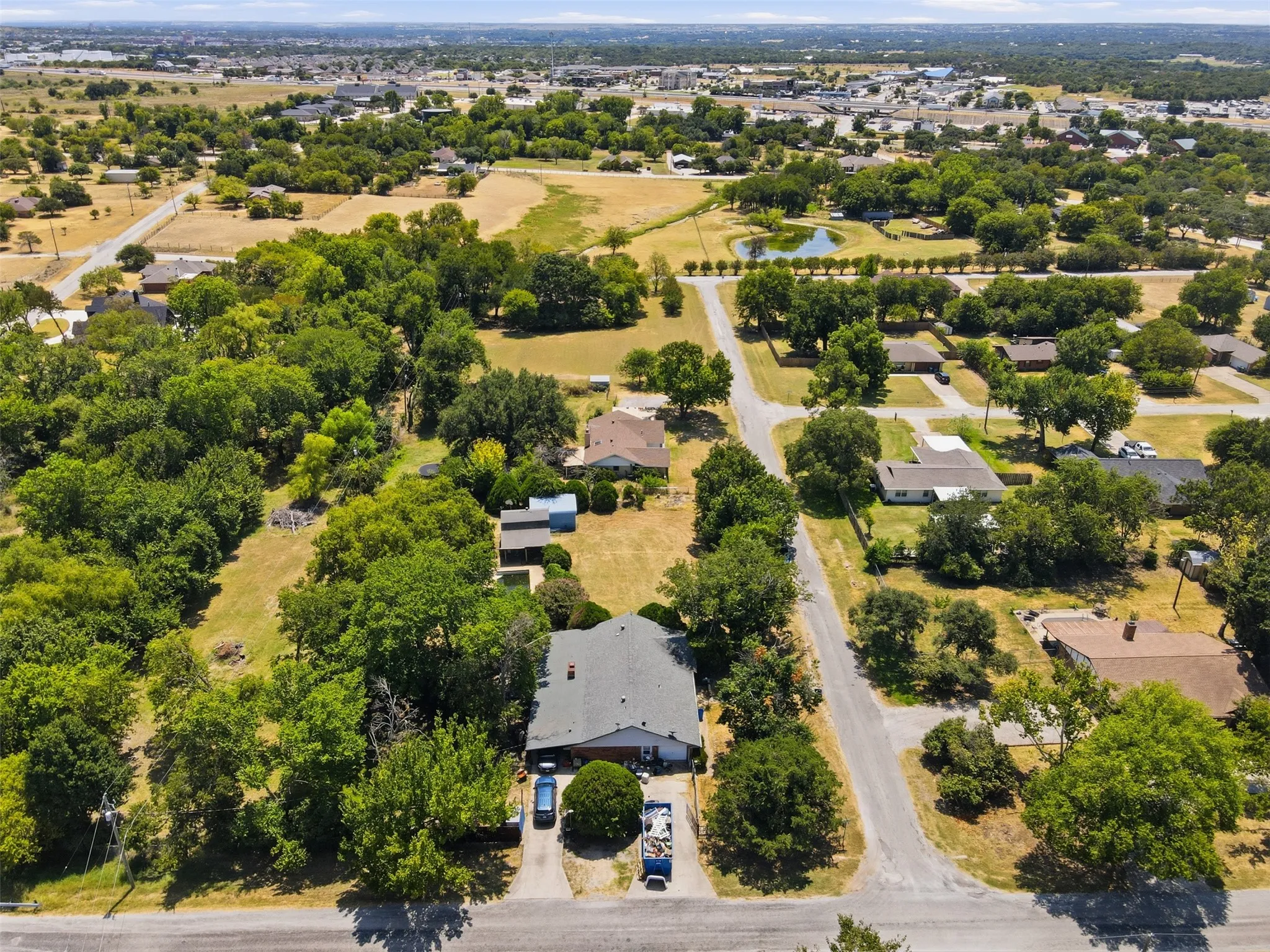 Residential area with mature trees, paved roads, and a visible pond feature