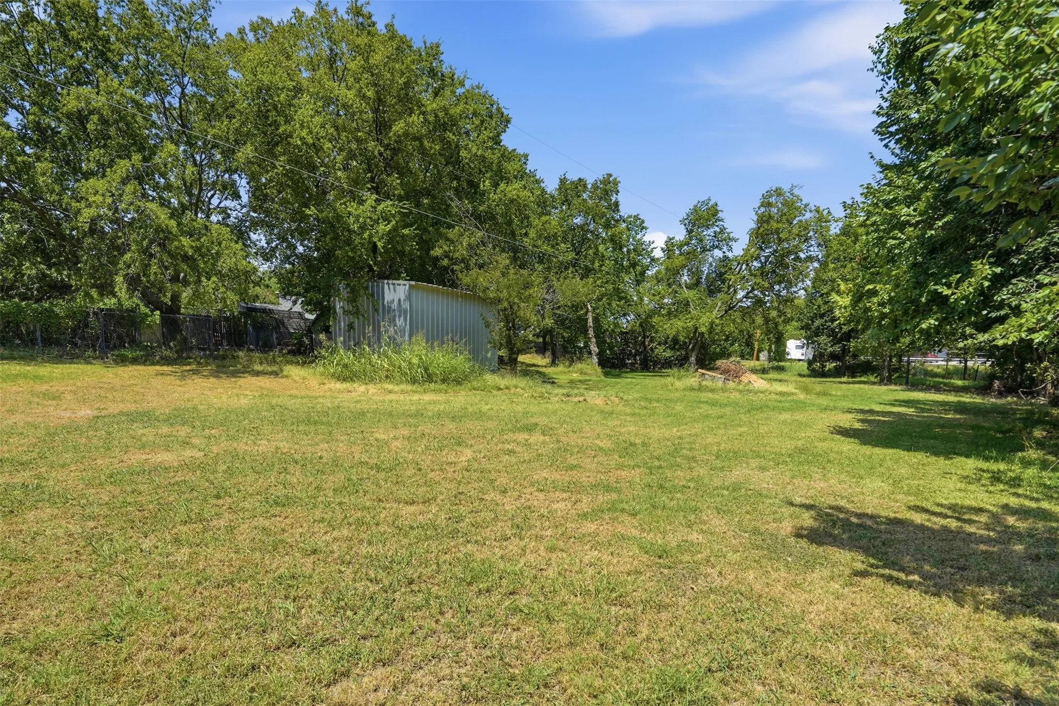 Expansive grassy lot with mature trees and a metal storage building