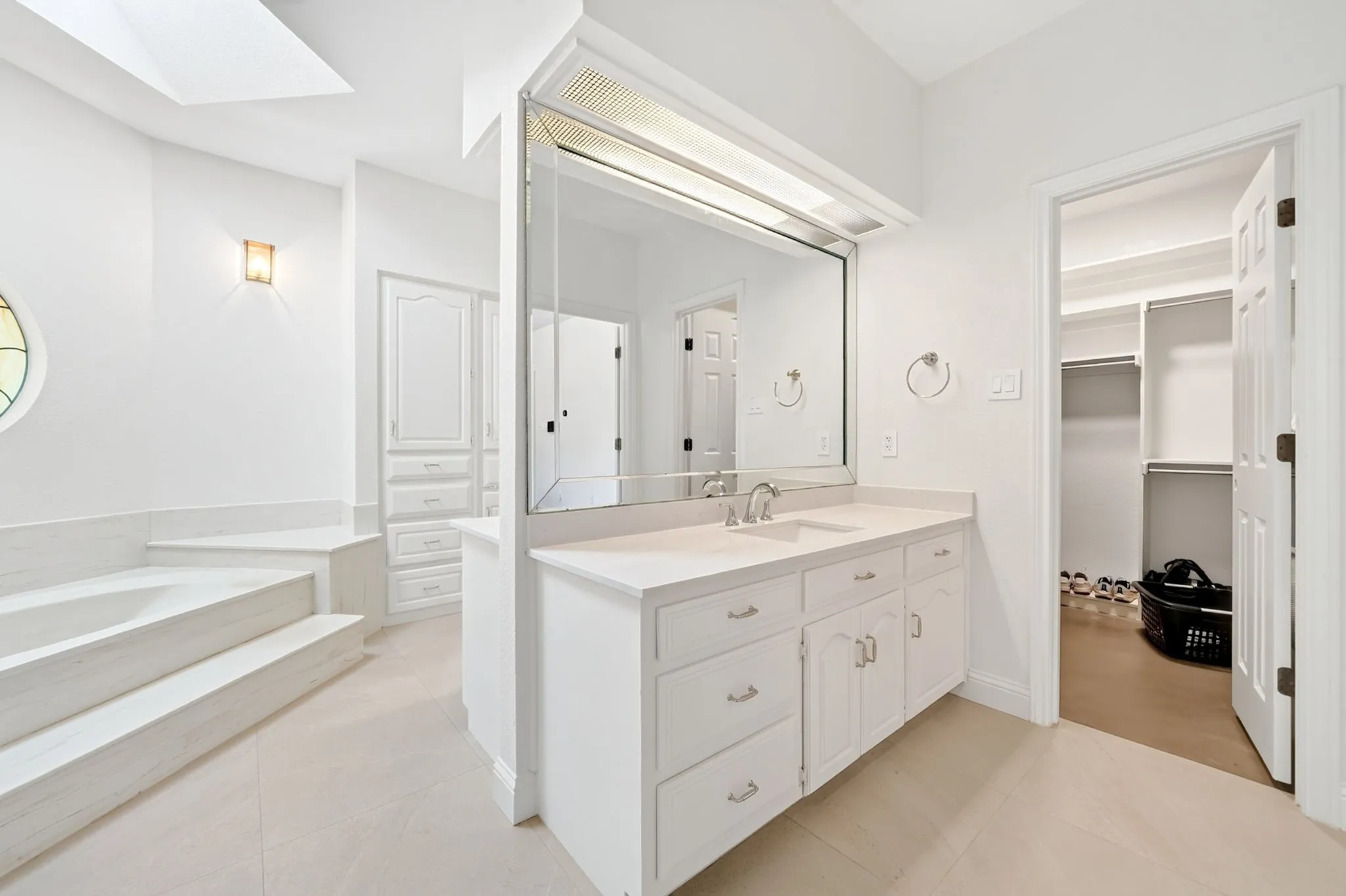 Integrated vanity with undermount sink, built-in storage cabinetry, tiled flooring, built-in tub with steps, and a skylight