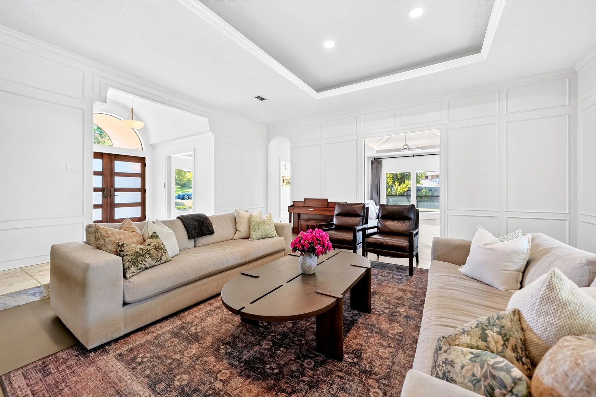 Formal living space featuring extensive wall paneling, a tray ceiling, recessed lighting, and a front entry door with horizontal lites