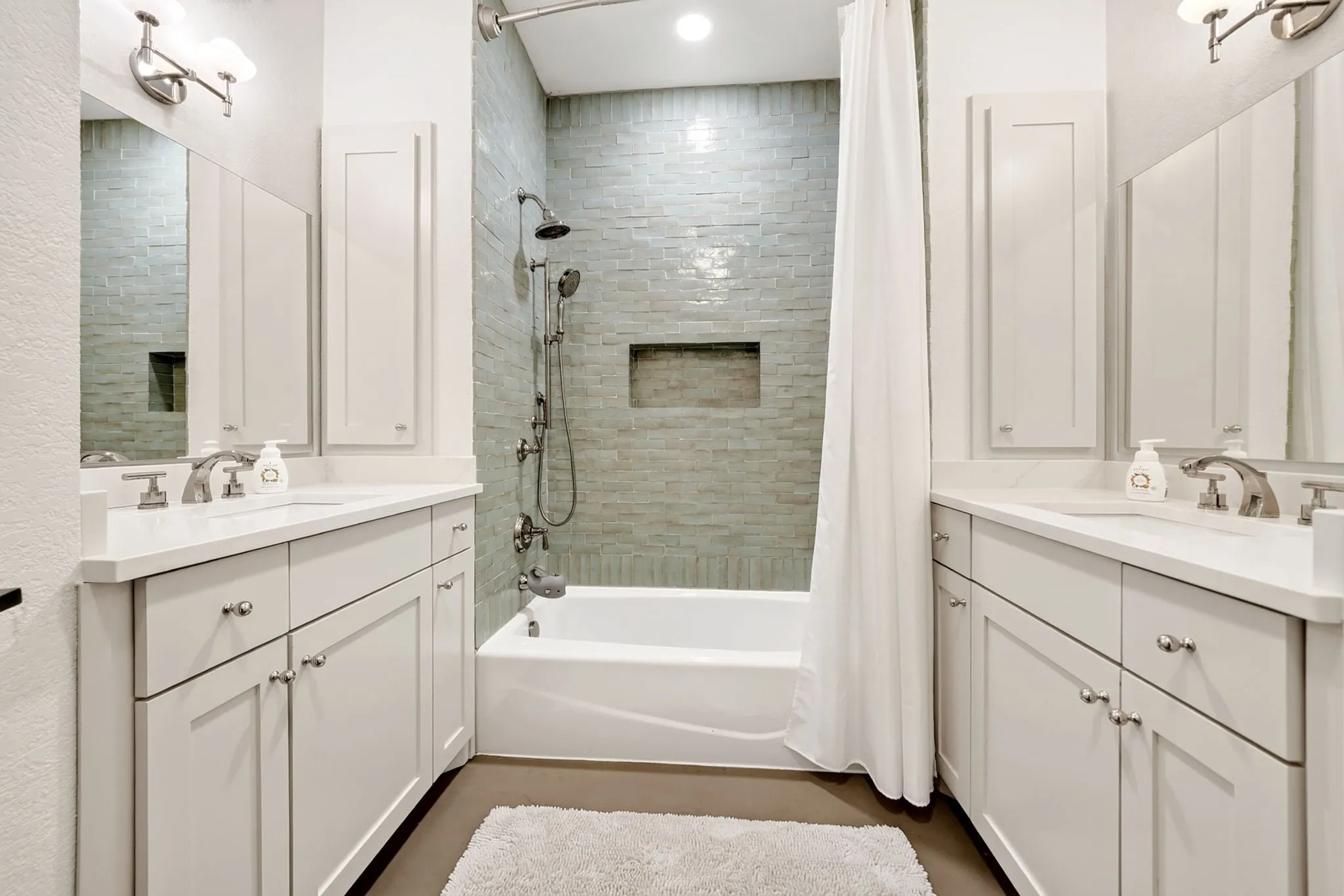 Dual vanity with white cabinetry and integrated sinks, a tiled shower/tub combination with a built-in niche, and brushed nickel fixtures