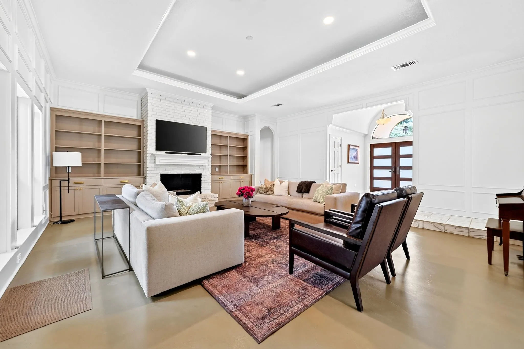 Recessed ceiling with integrated lighting, built-in shelving, brick fireplace, wood-finish flooring, and panel molding