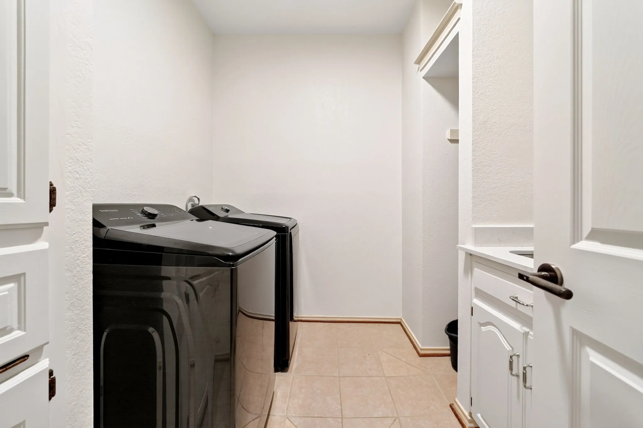 Laundry area featuring tile flooring, white cabinetry, and an integrated sink with a countertop