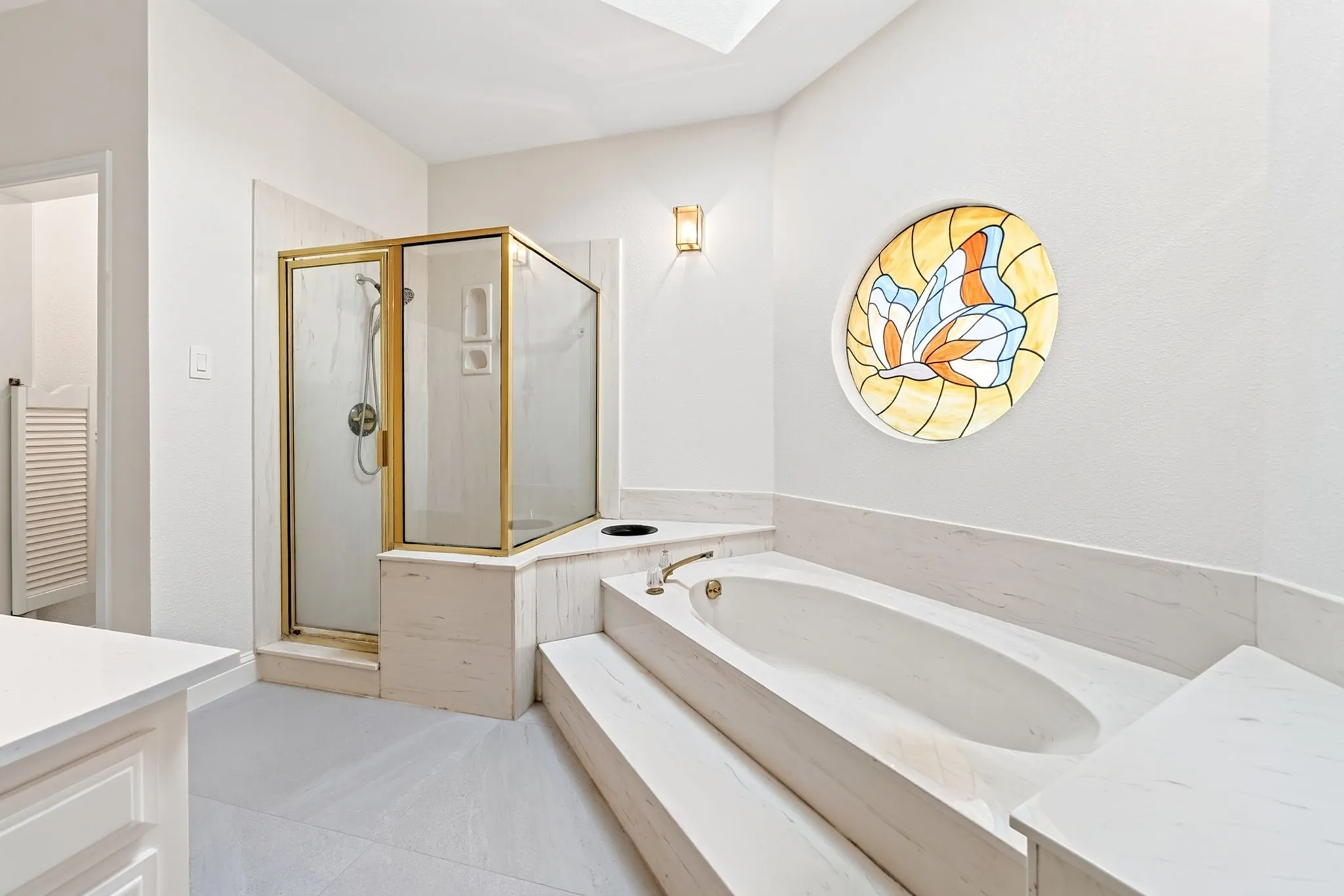 Built-in soaking tub with tiered steps, separate shower with brass-finish enclosure, and a round stained-glass window