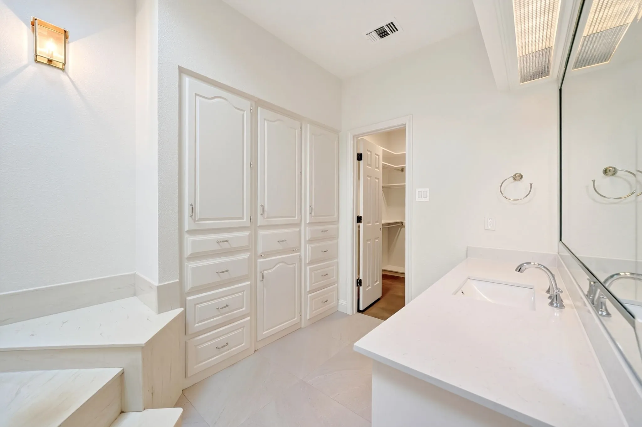Integrated vanity with an undermount sink, a large wall-mounted mirror, and white cabinetry with drawer storage