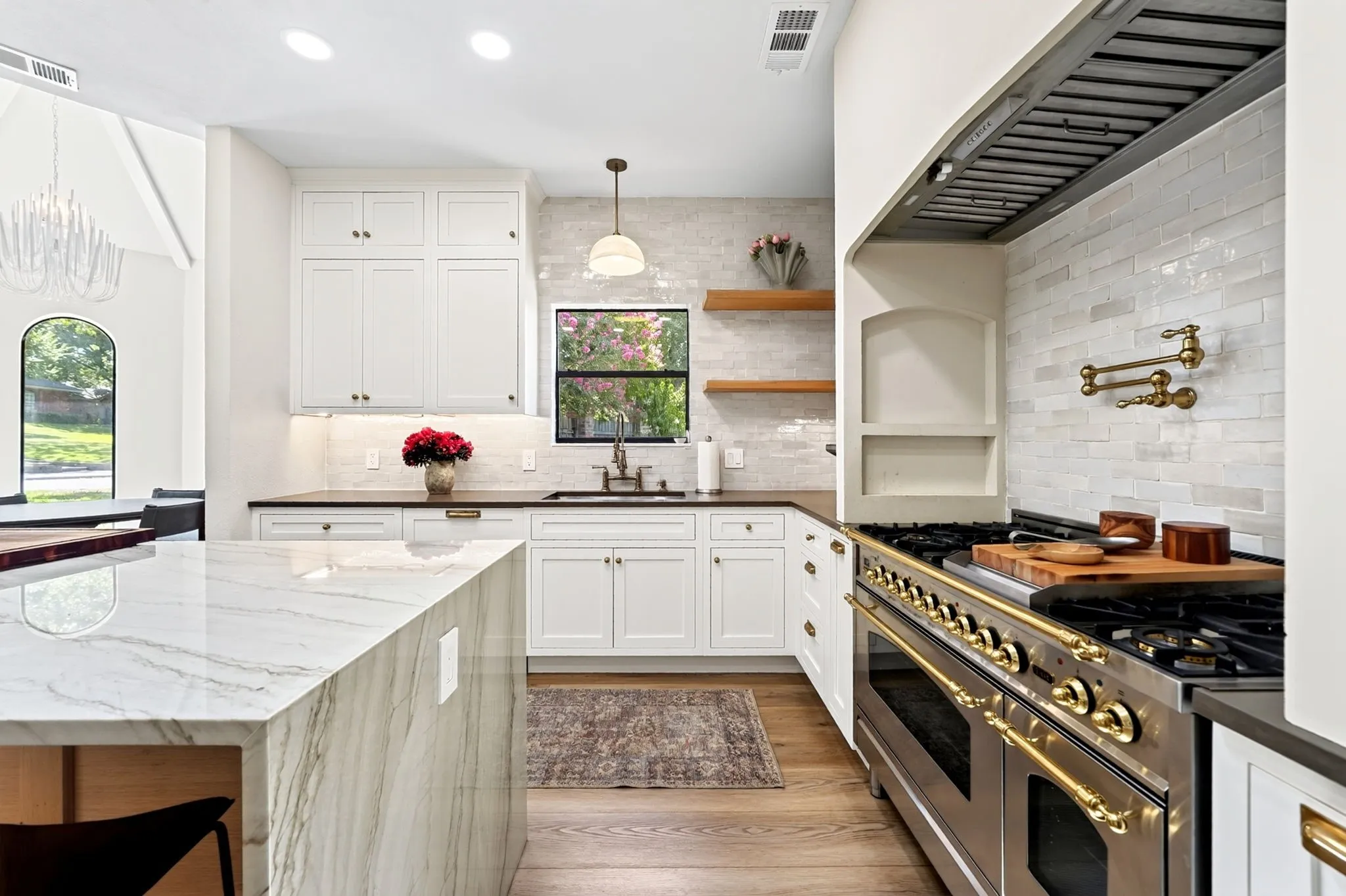 Gourmet kitchen with a large range and gold-tone hardware, white shaker cabinetry, stone countertops, wood-finish flooring, and a waterfall island