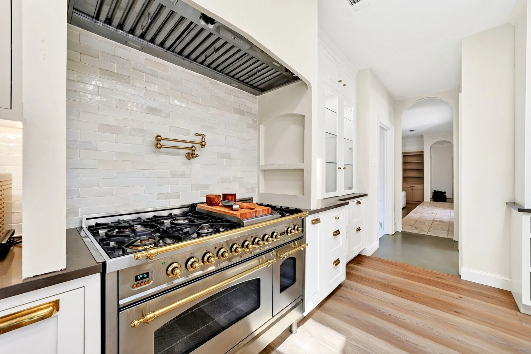 Professional-grade range with brass accents, white subway tile backsplash, under-cabinet lighting, wood-finish flooring, and arched doorways
