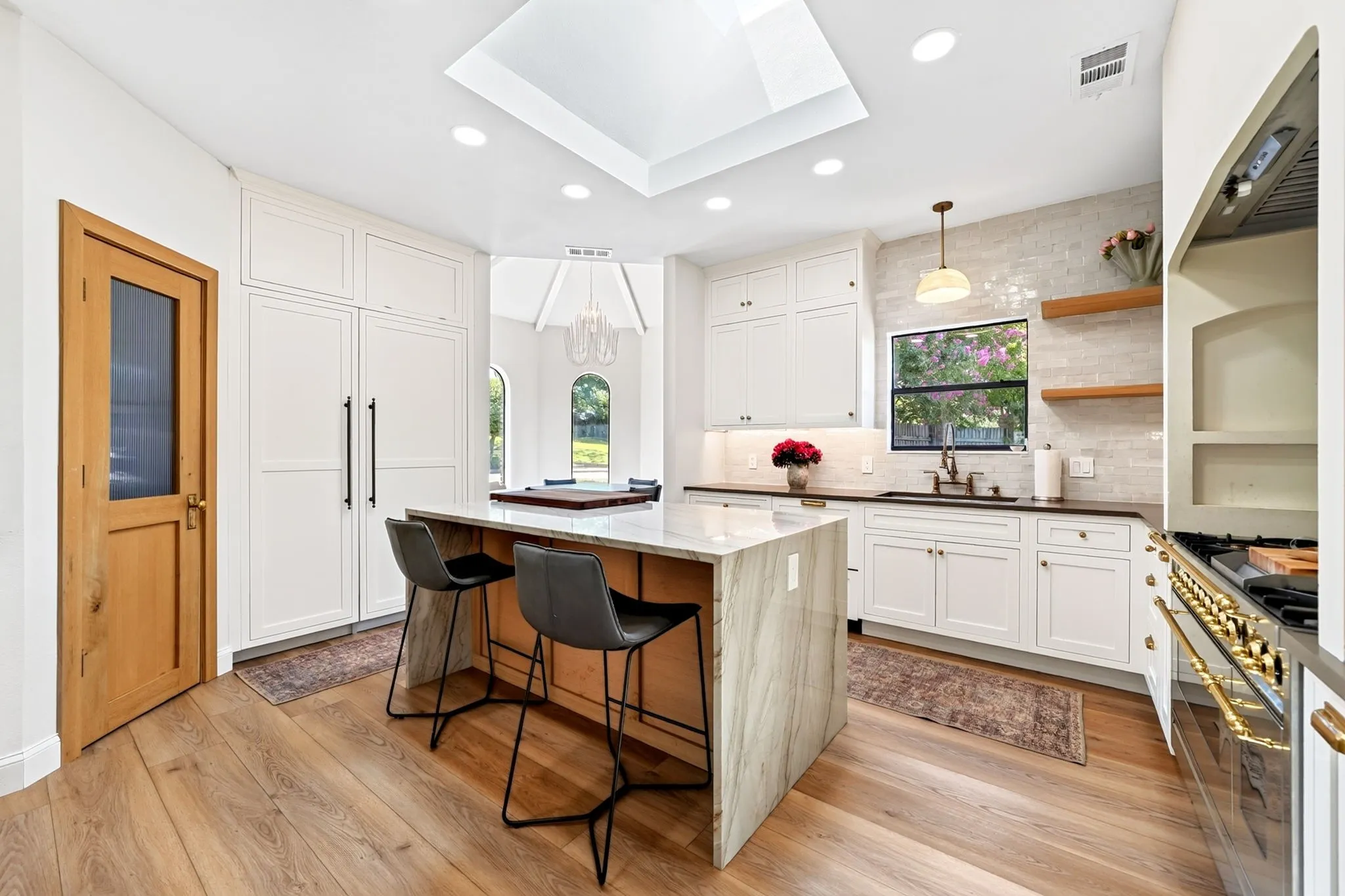 Gourmet kitchen with wood-finish flooring, white cabinetry, a skylight, a central island with a waterfall countertop, and a built-in range
