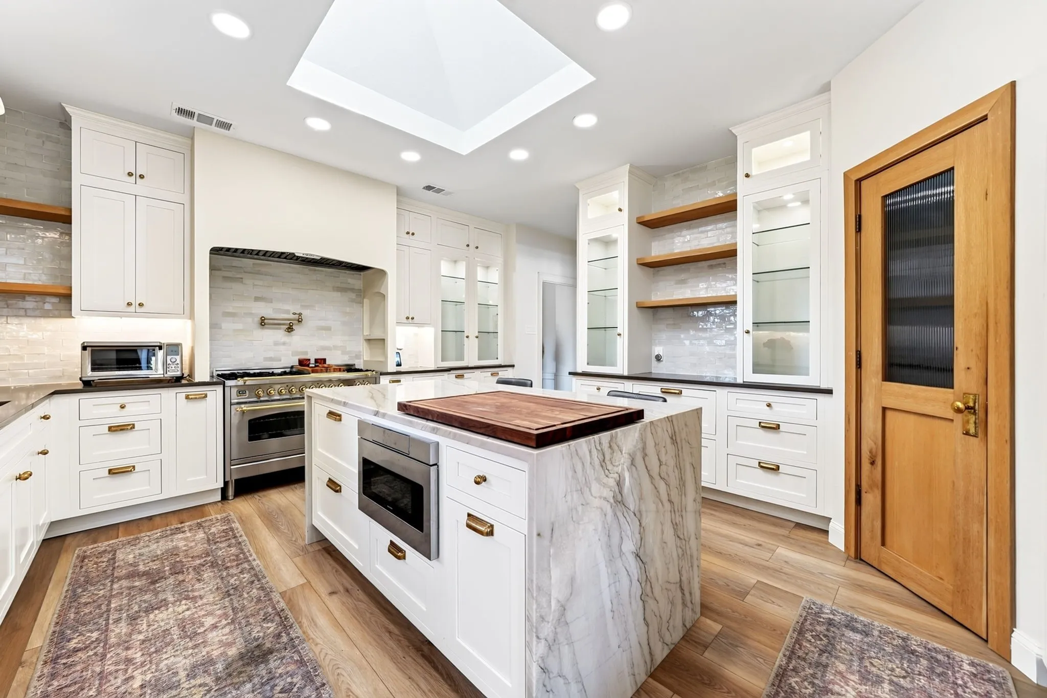 Kitchen featuring a skylight, recessed lighting, white cabinetry, a large kitchen island with integrated microwave, and wood-finish flooring