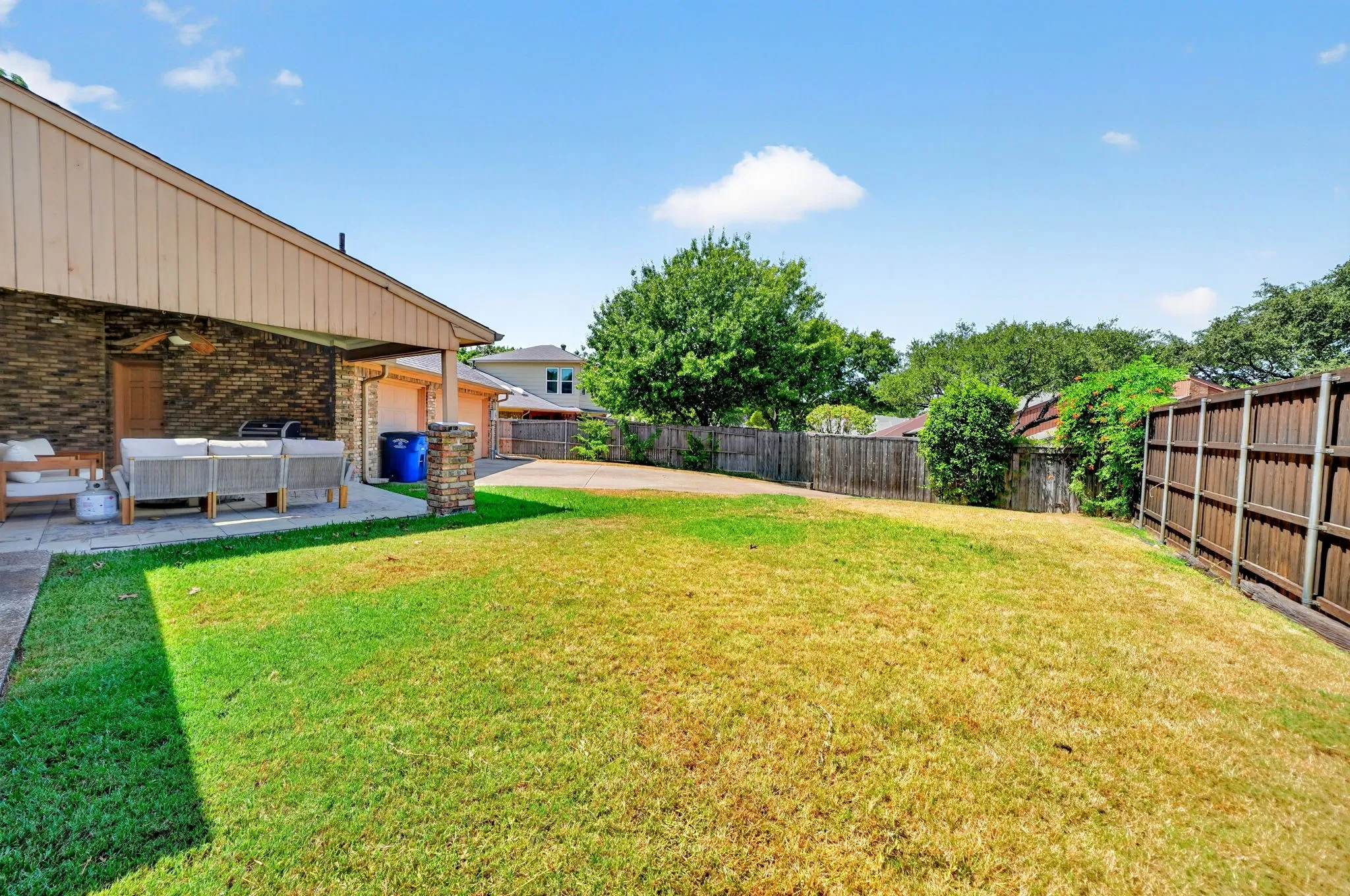 Expansive backyard featuring a covered patio, brick exterior, wood privacy fencing, and mature landscaping