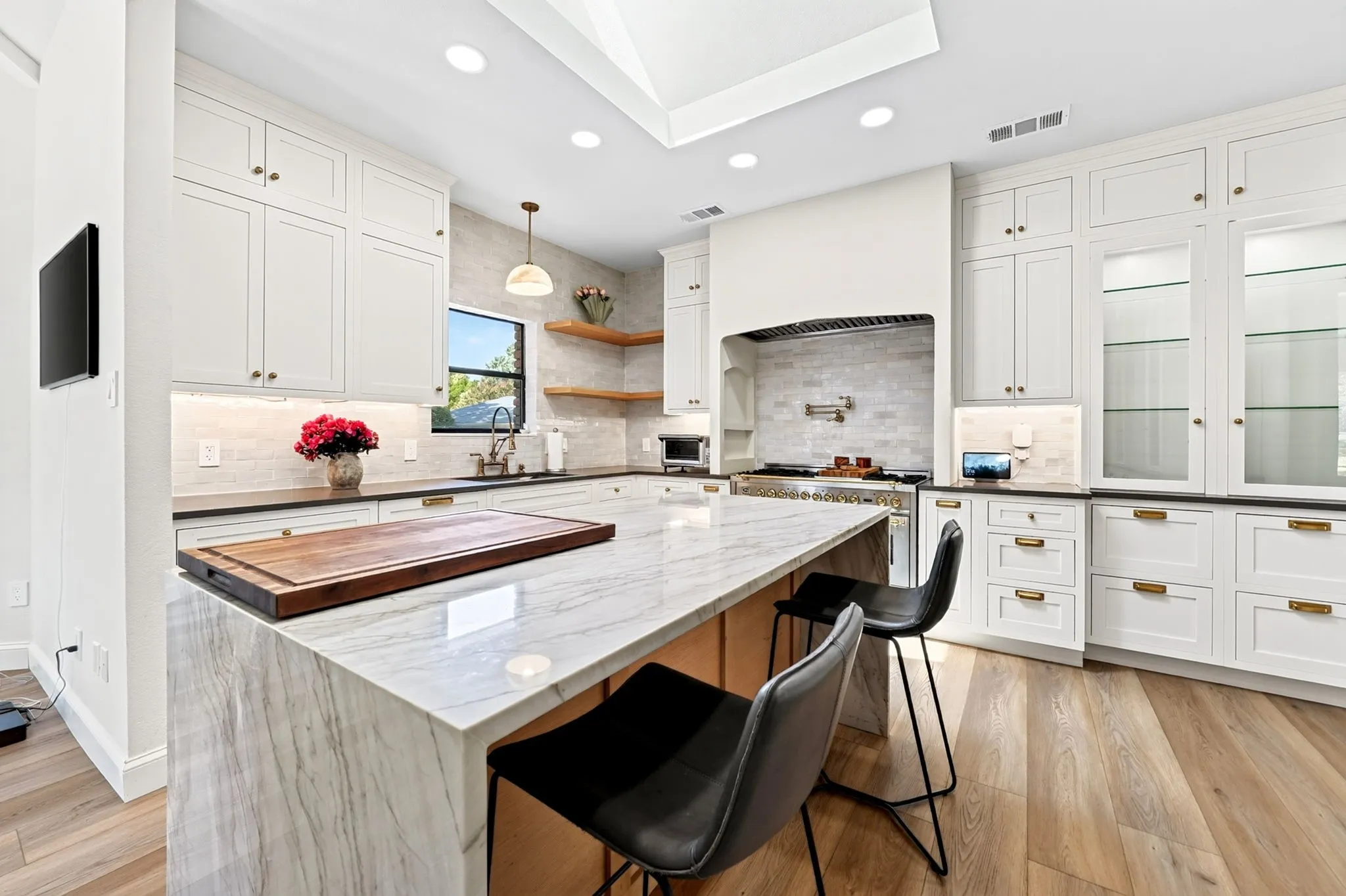 Center island with stone countertop, extensive white cabinetry, wood-finish flooring, recessed lighting, and a skylight