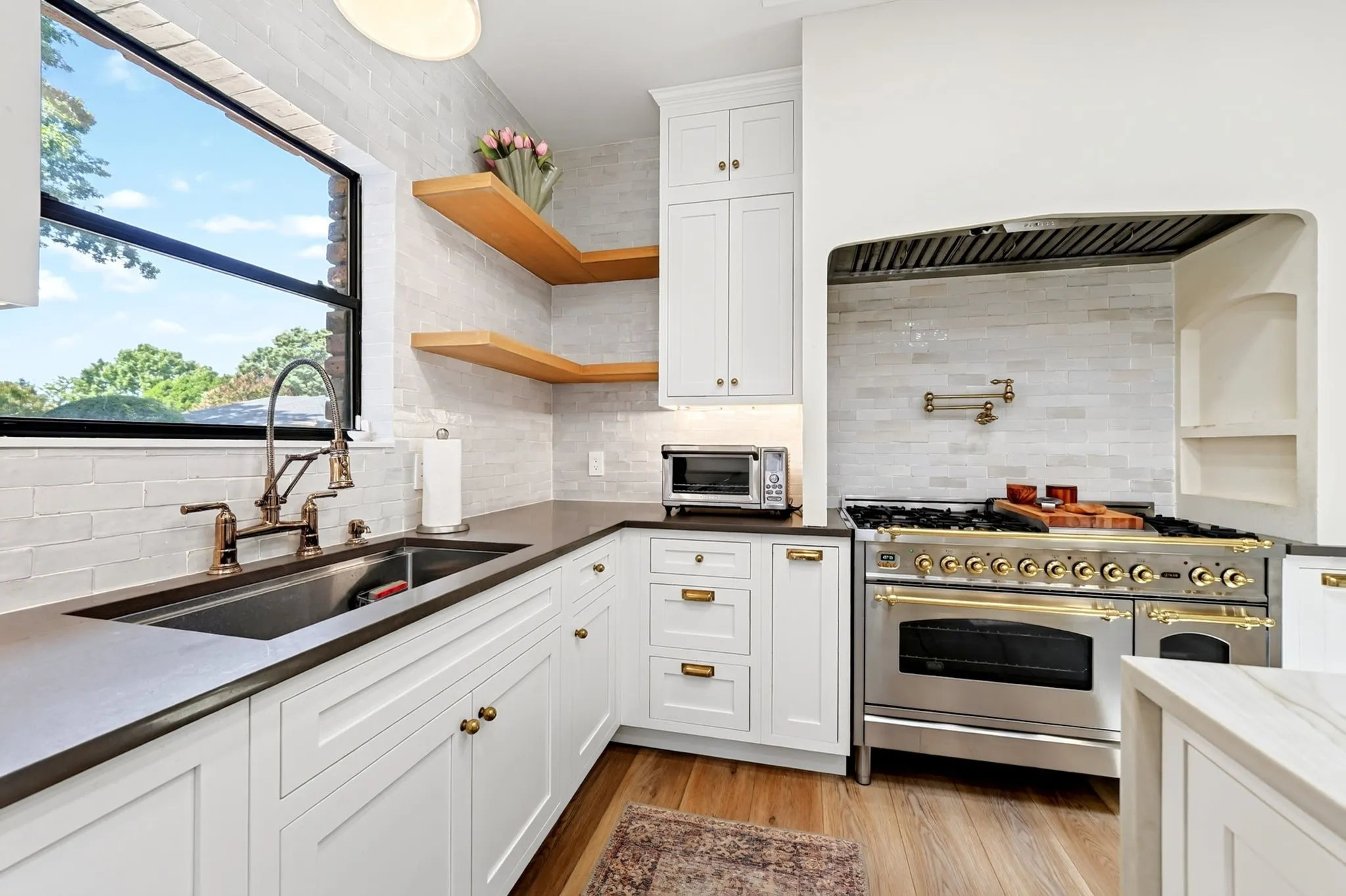 Gourmet kitchen featuring a stainless steel range, white shaker cabinetry, dark countertops, wood-finish flooring, and open wood shelving