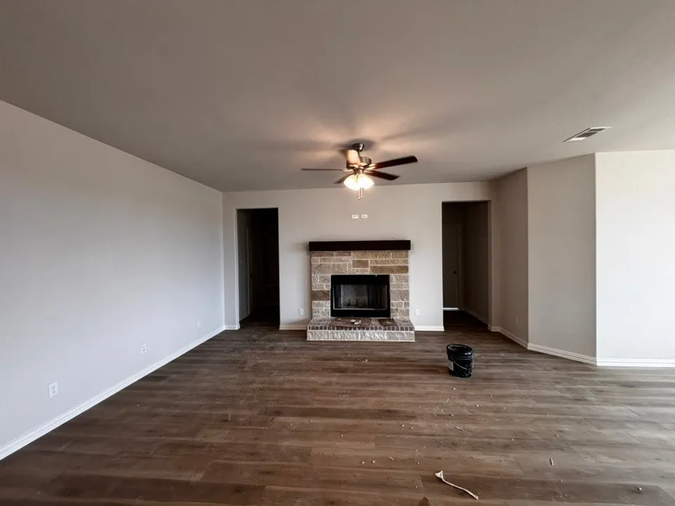 Living area featuring wood-finish flooring, a stone-faced fireplace with a hearth and dark wood mantel, and a ceiling fan with integrated lighting