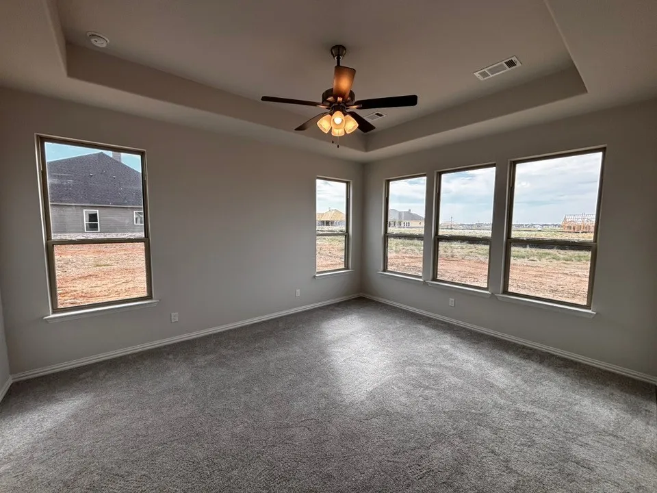 Tray ceiling with recessed lighting, ceiling fan, grey carpeting, and multiple windows