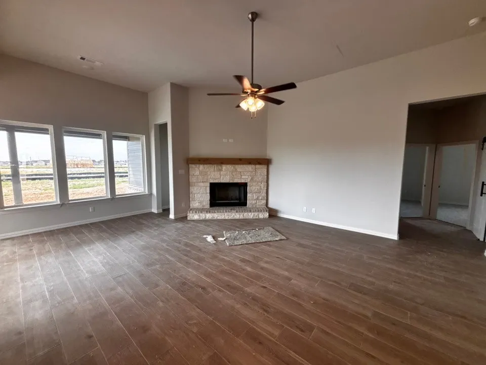 Vaulted ceilings with a ceiling fan, wood-finish flooring, stone fireplace with a wood mantle, and multiple windows